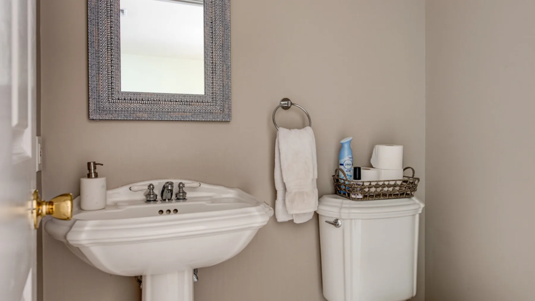 Un baño con lavabo de pedestal, espejo de pared e inodoro.