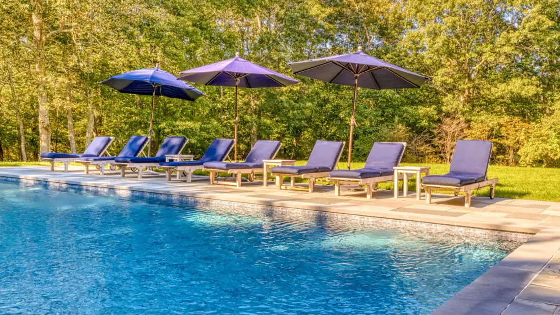 An outdoor swimming pool with lounge chairs and umbrellas beside it.