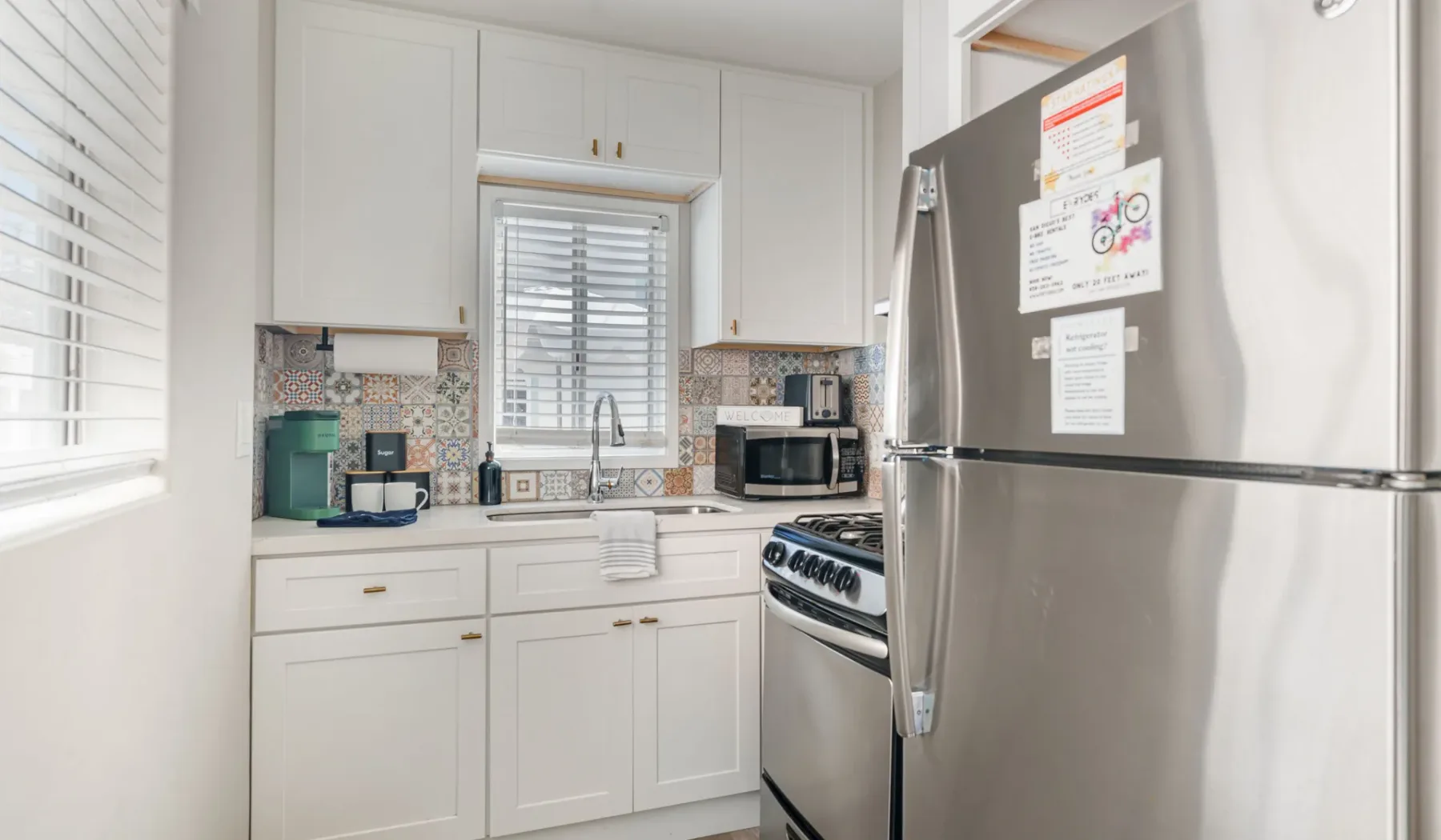 A bright kitchen with white cabinets, a refrigerator, and a stove.