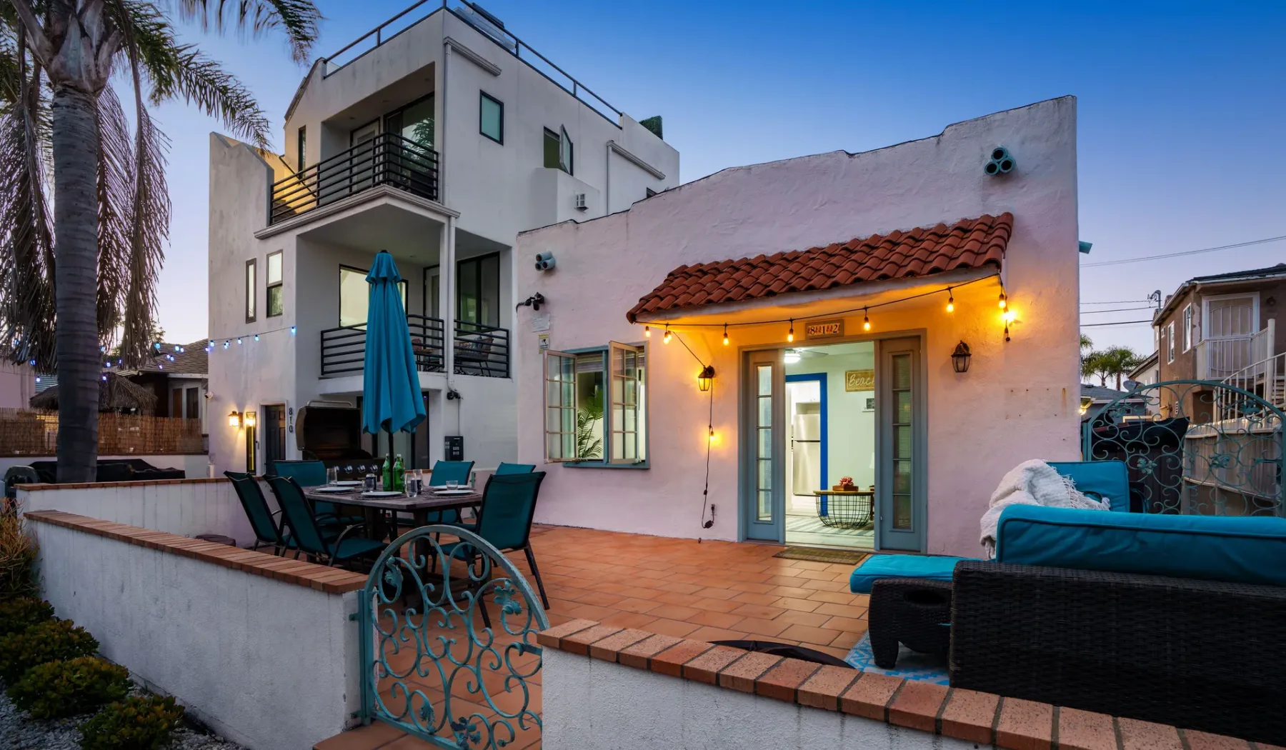 A modern house opens onto a tiled patio with outdoor seating and a small pool.