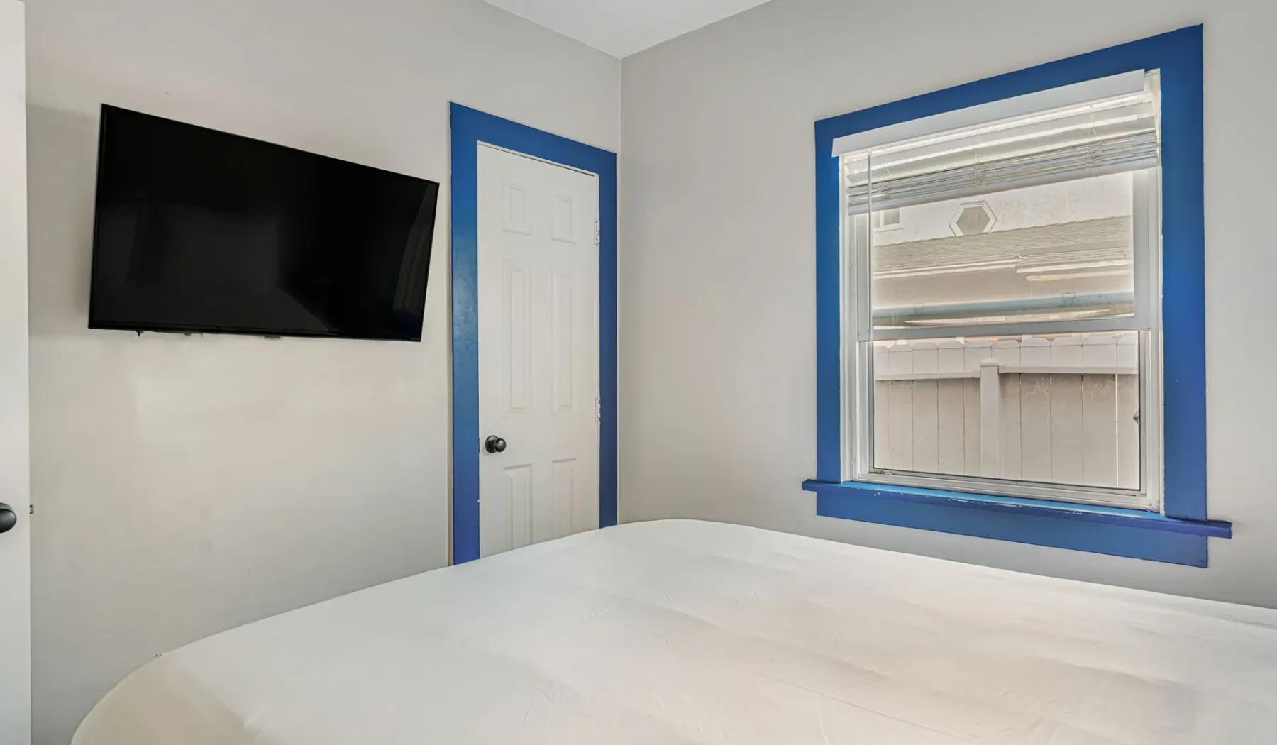A bedroom with a bed, wall-mounted television, and window.