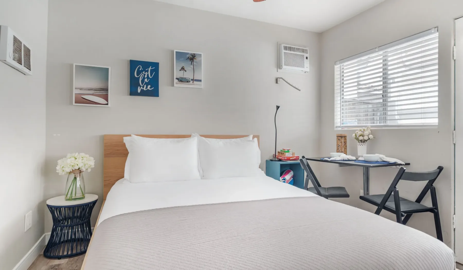 A bright bedroom with a neatly made bed and a small table beside the window.