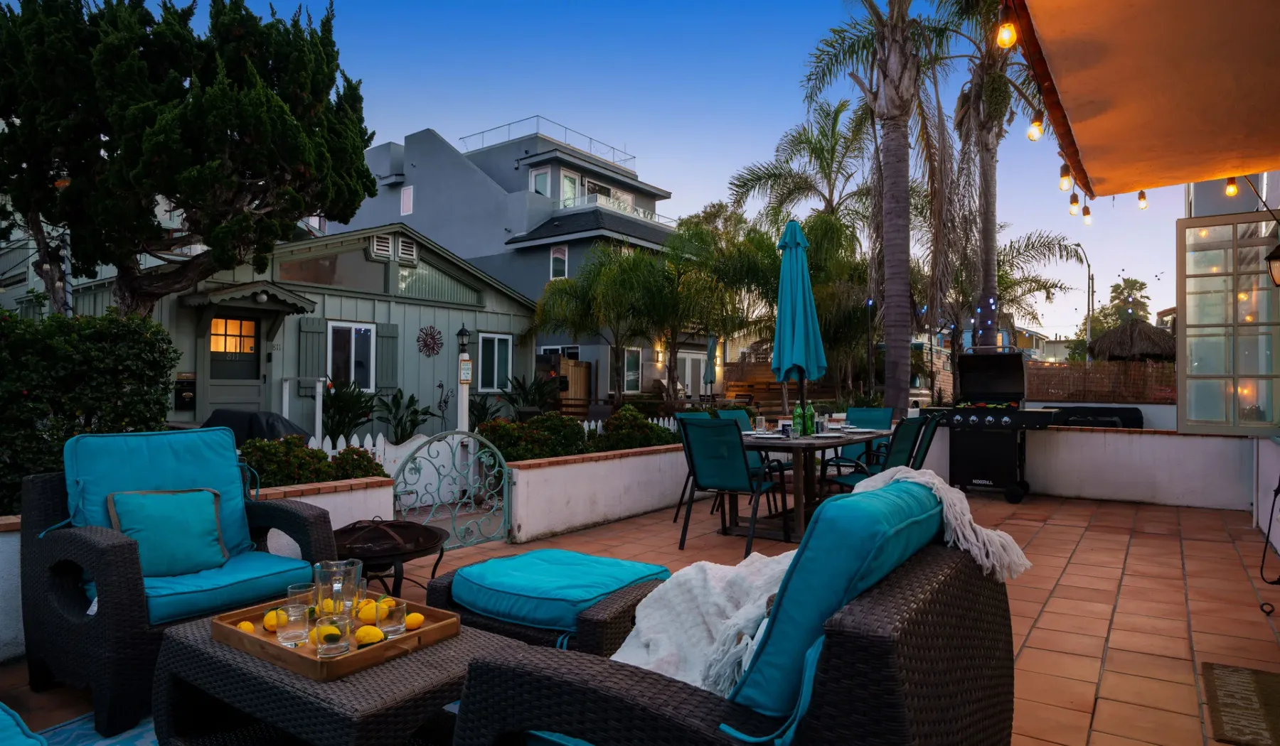 An outdoor patio with seating, a dining table, and palm trees at dusk.