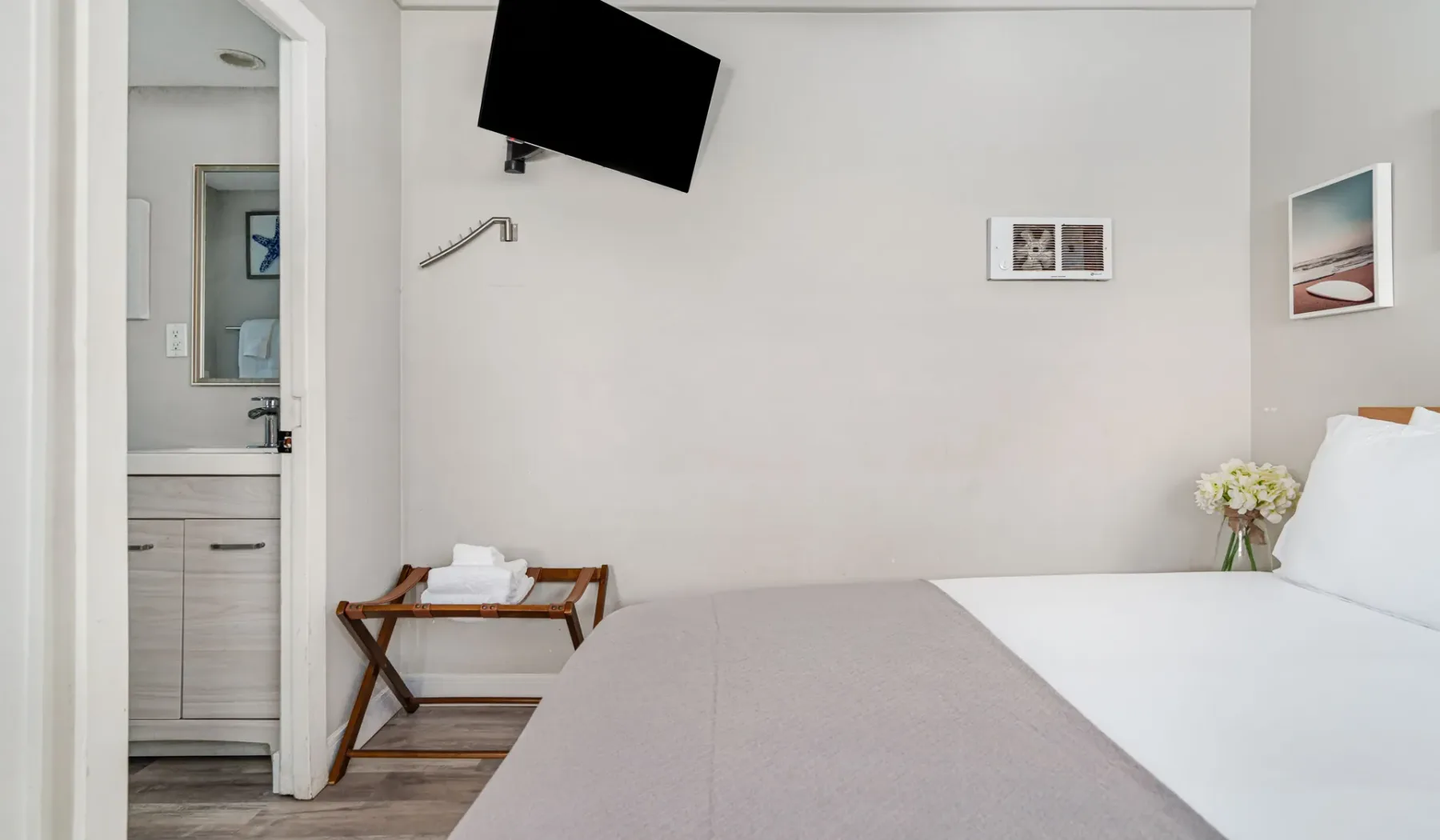 A bedroom with a neatly made bed and a wall-mounted television.