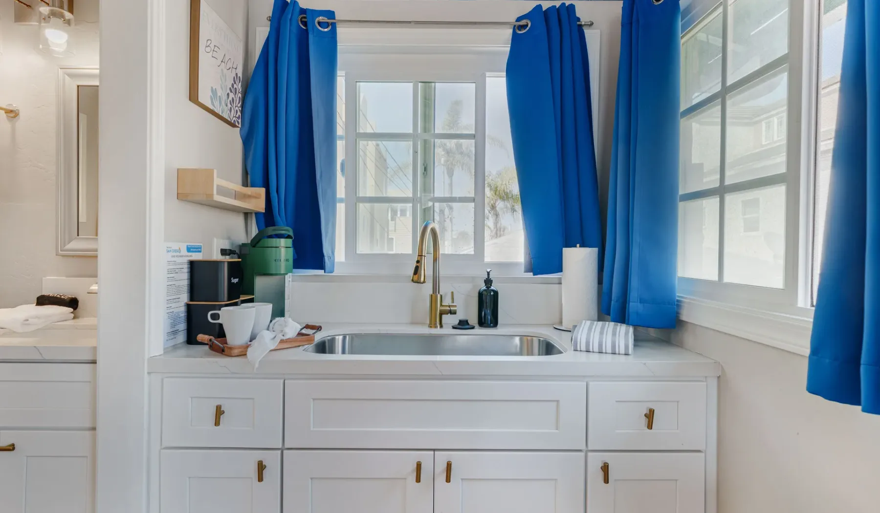 A bright kitchen with a sink beneath windows framed by blue curtains.
