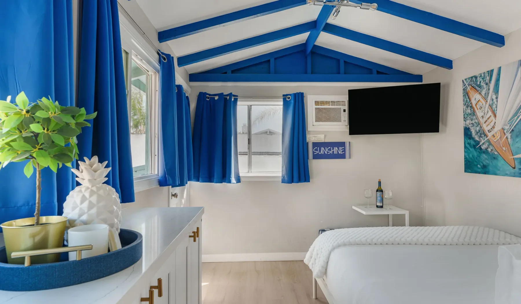 A bright bedroom with blue ceiling beams, a bed, and windows.