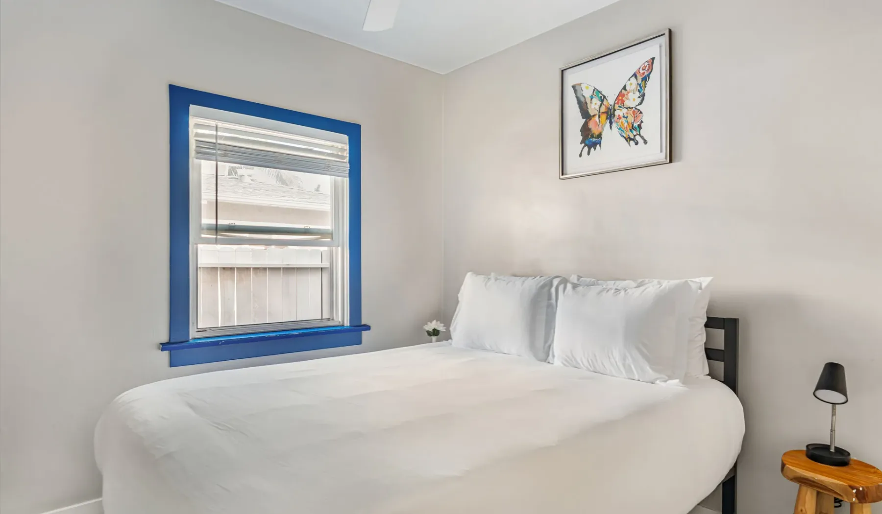 A bedroom with a bed, blue-trimmed window, and framed butterfly artwork.