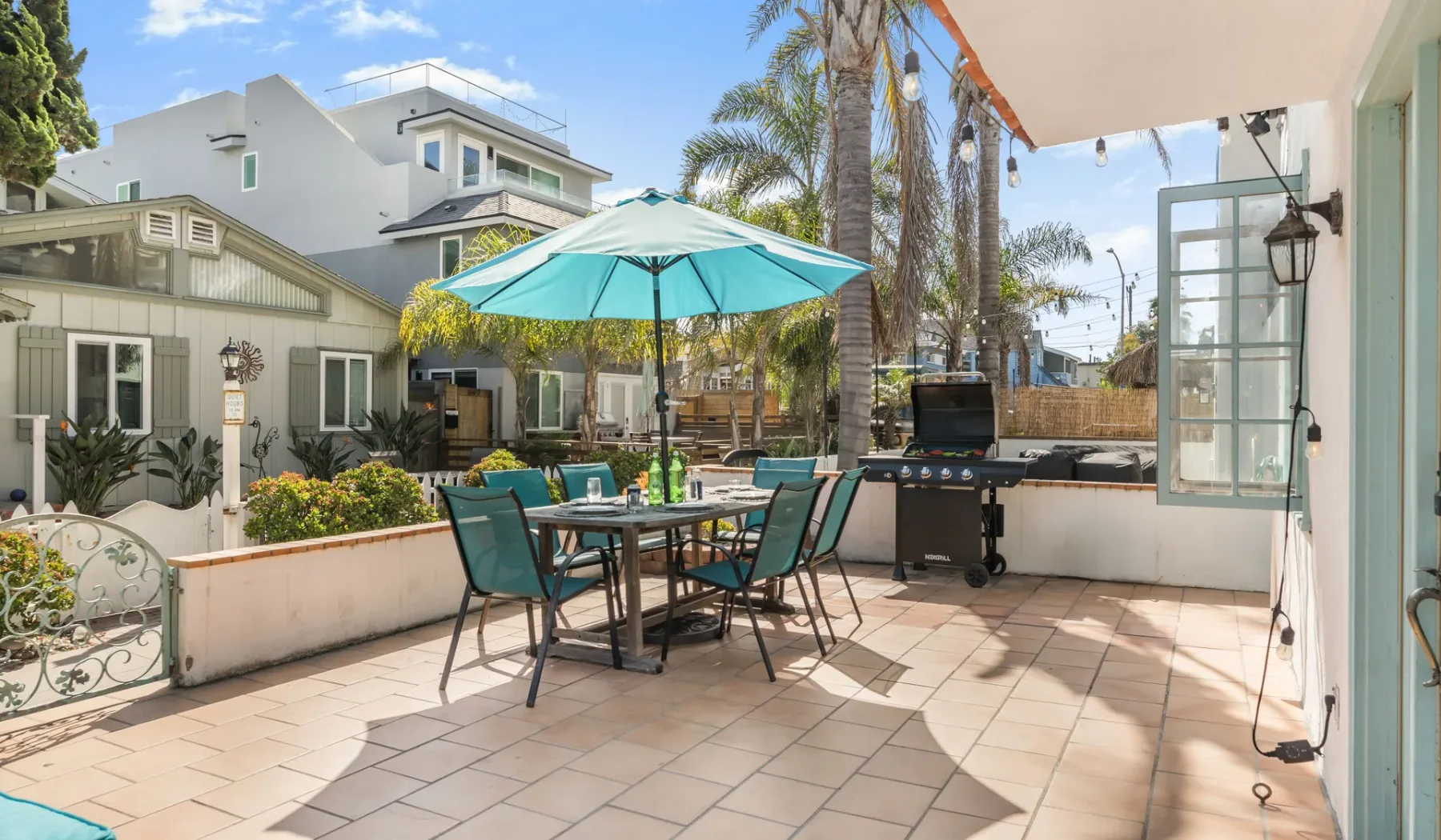 A sunny outdoor patio with a dining table, umbrella, and grill.