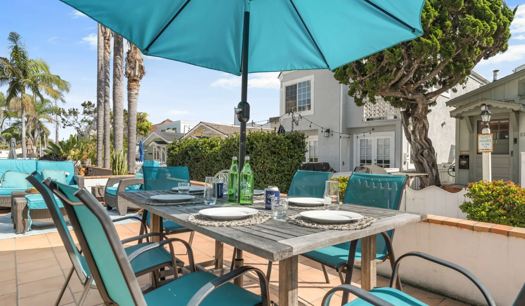 An outdoor patio dining area with tables and teal seating beneath a large umbrella.