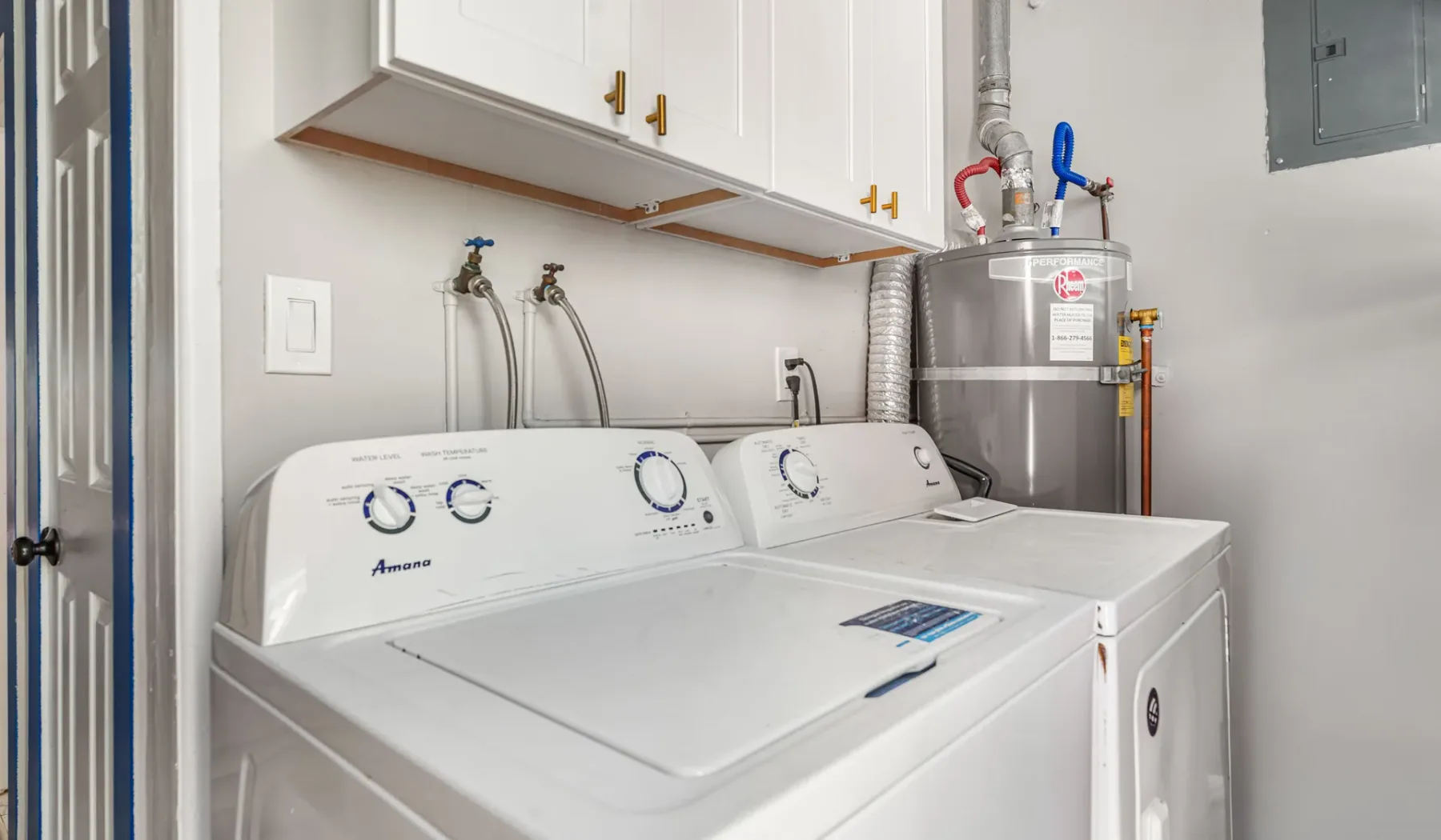 A laundry room with a washer and dryer beneath white cabinets.