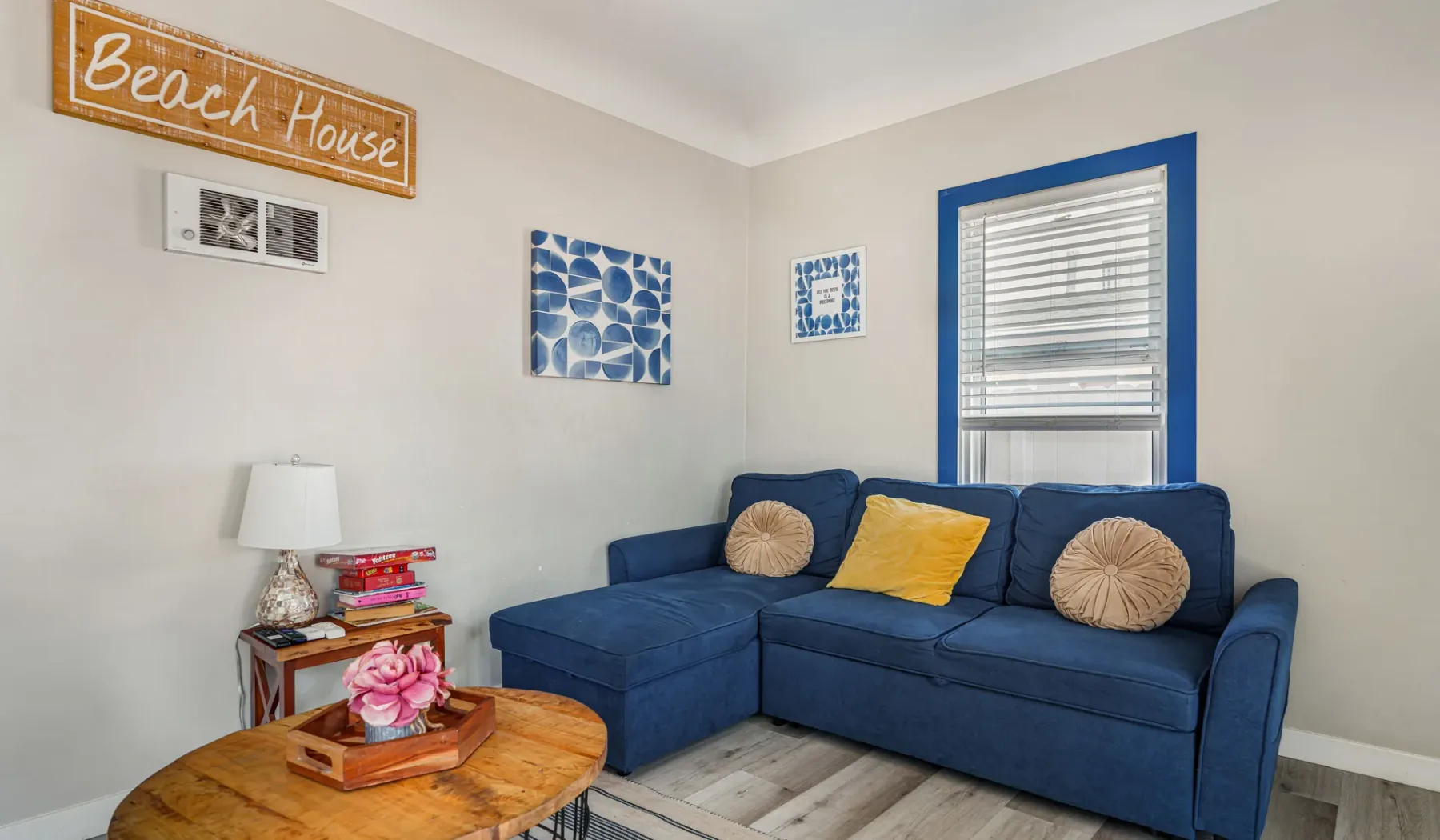 A living room with blue seating and colorful cushions beneath a window.
