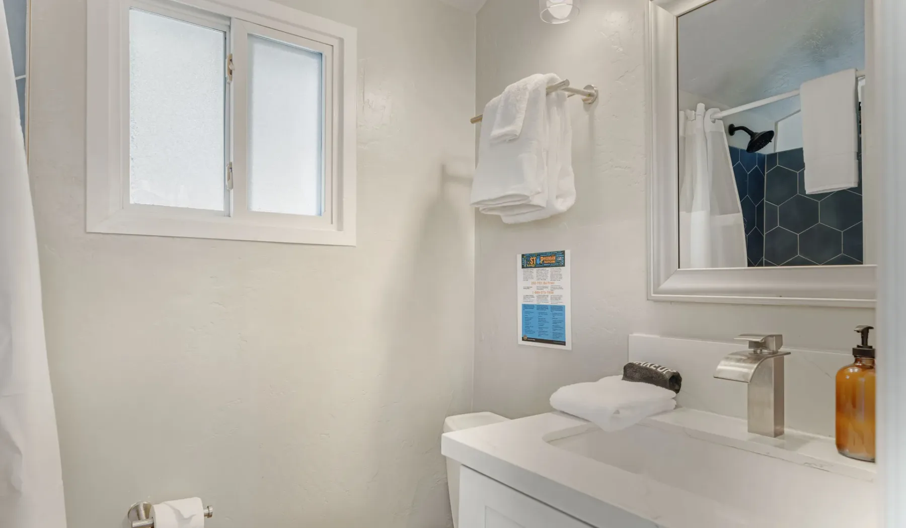 A bright bathroom with a vanity, sink, and shower visible in the mirror.