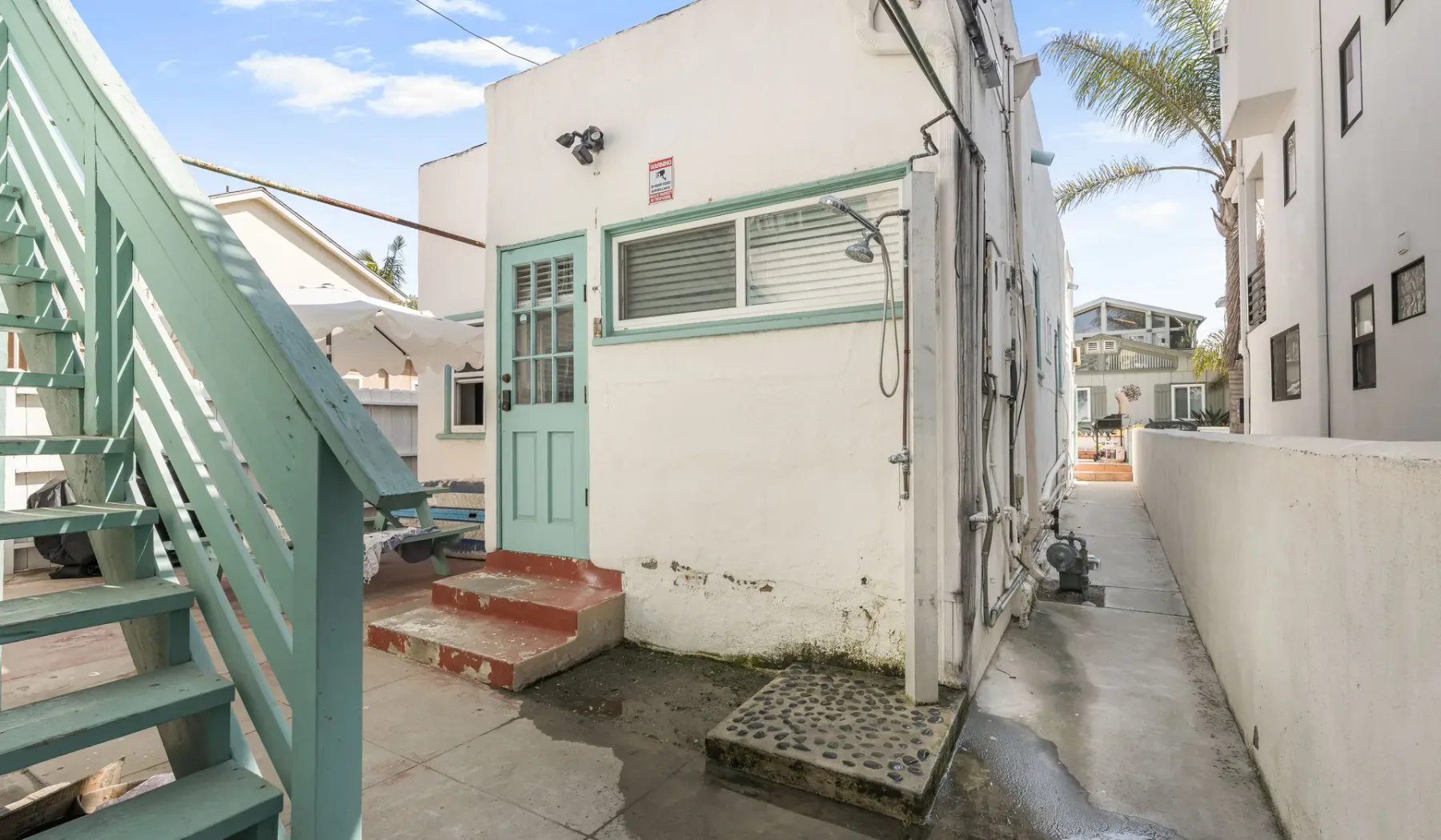 An outdoor passage beside a white building, with a pale green exterior staircase and door.