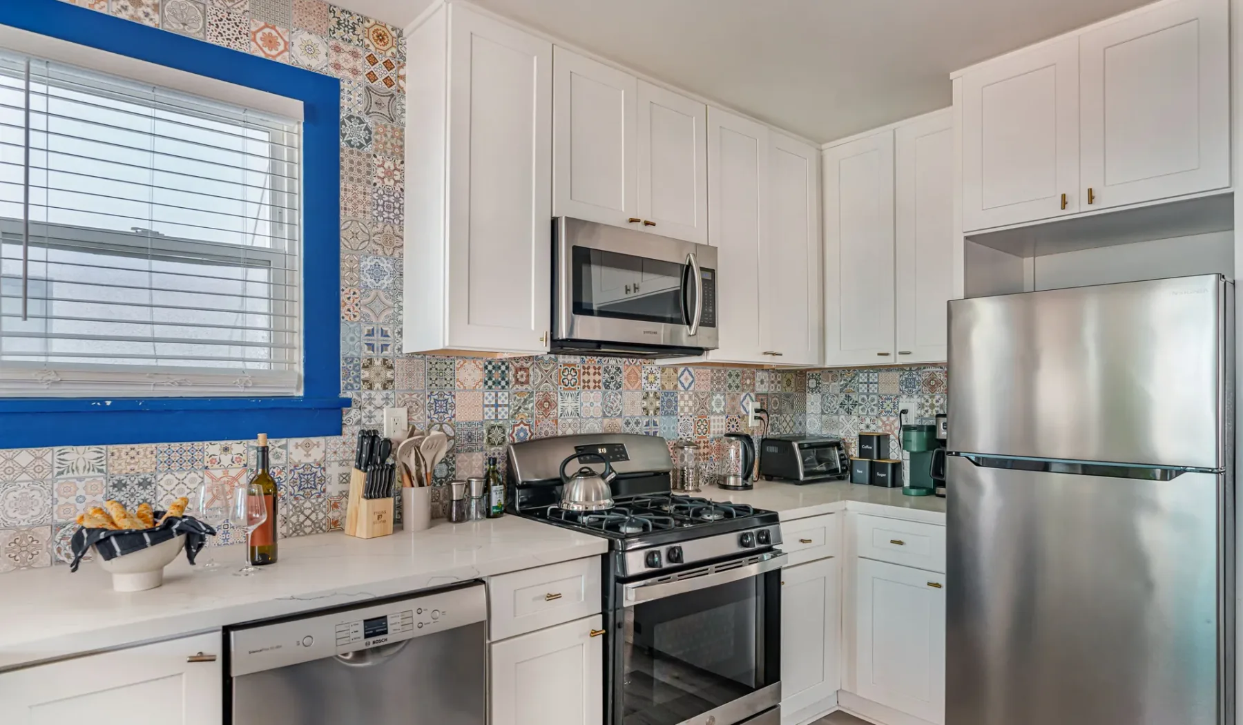 A bright kitchen with white cabinets, stainless steel appliances, and patterned tile.