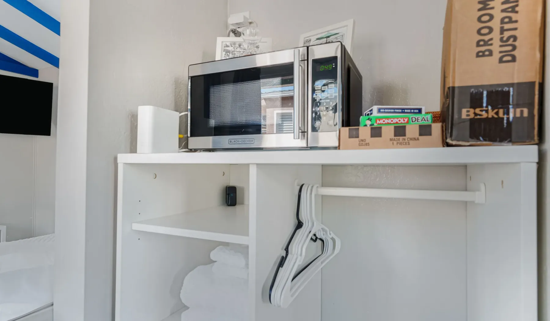 A white shelving unit holds a microwave, with hangers and folded towels below.