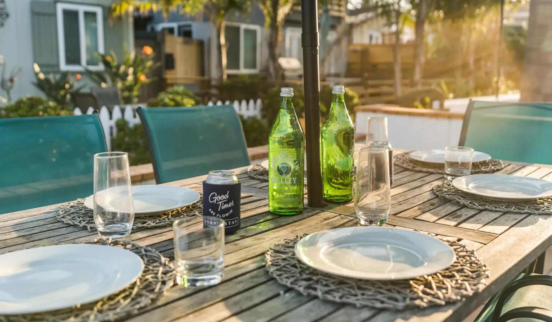 An outdoor dining table is set with plates, glasses, and green bottles.