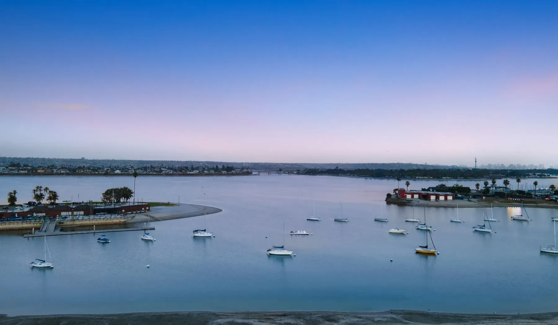 A calm harbor with sailboats anchored across the water.