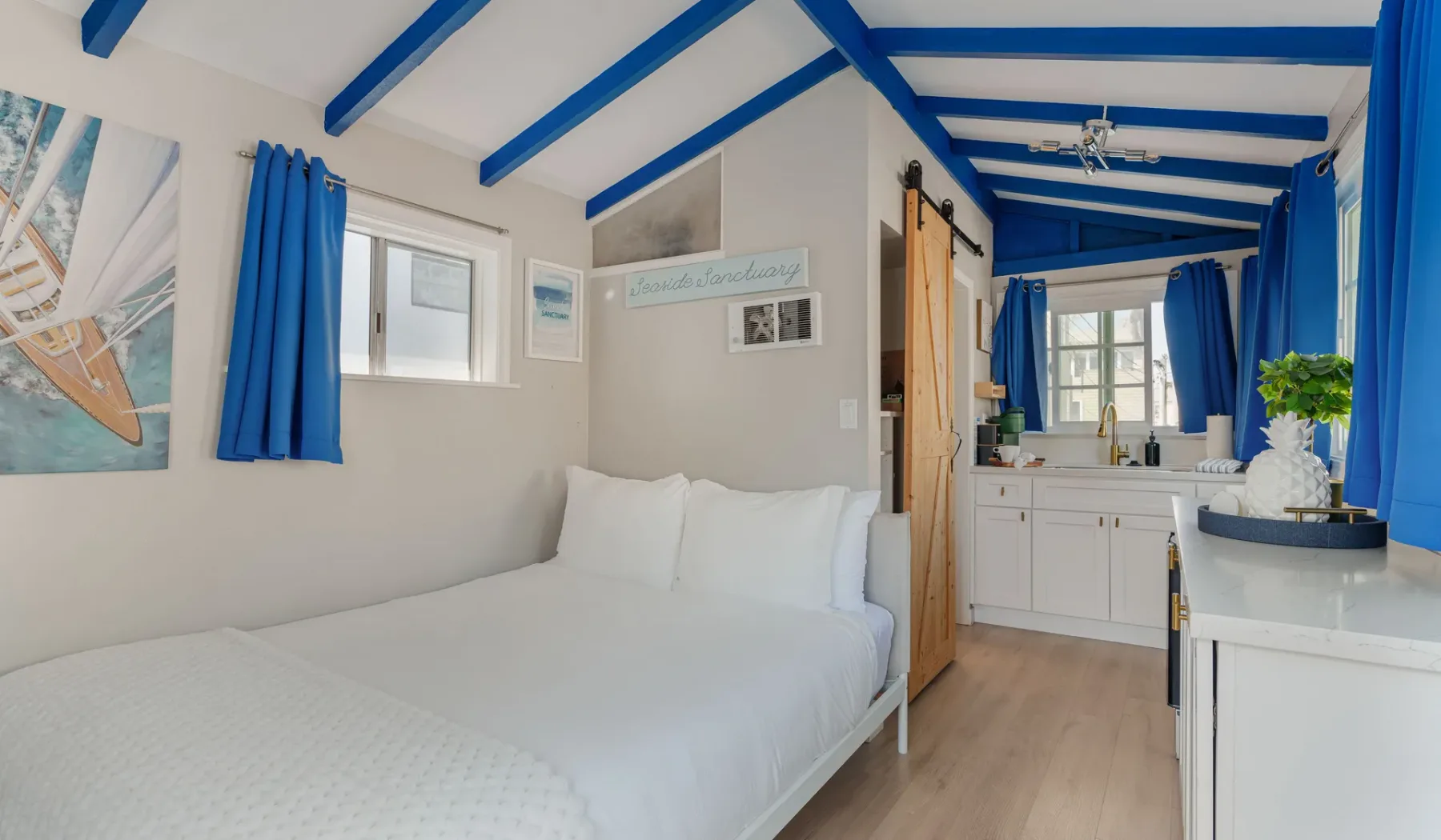 A bright bedroom with a white bed and blue ceiling beams.