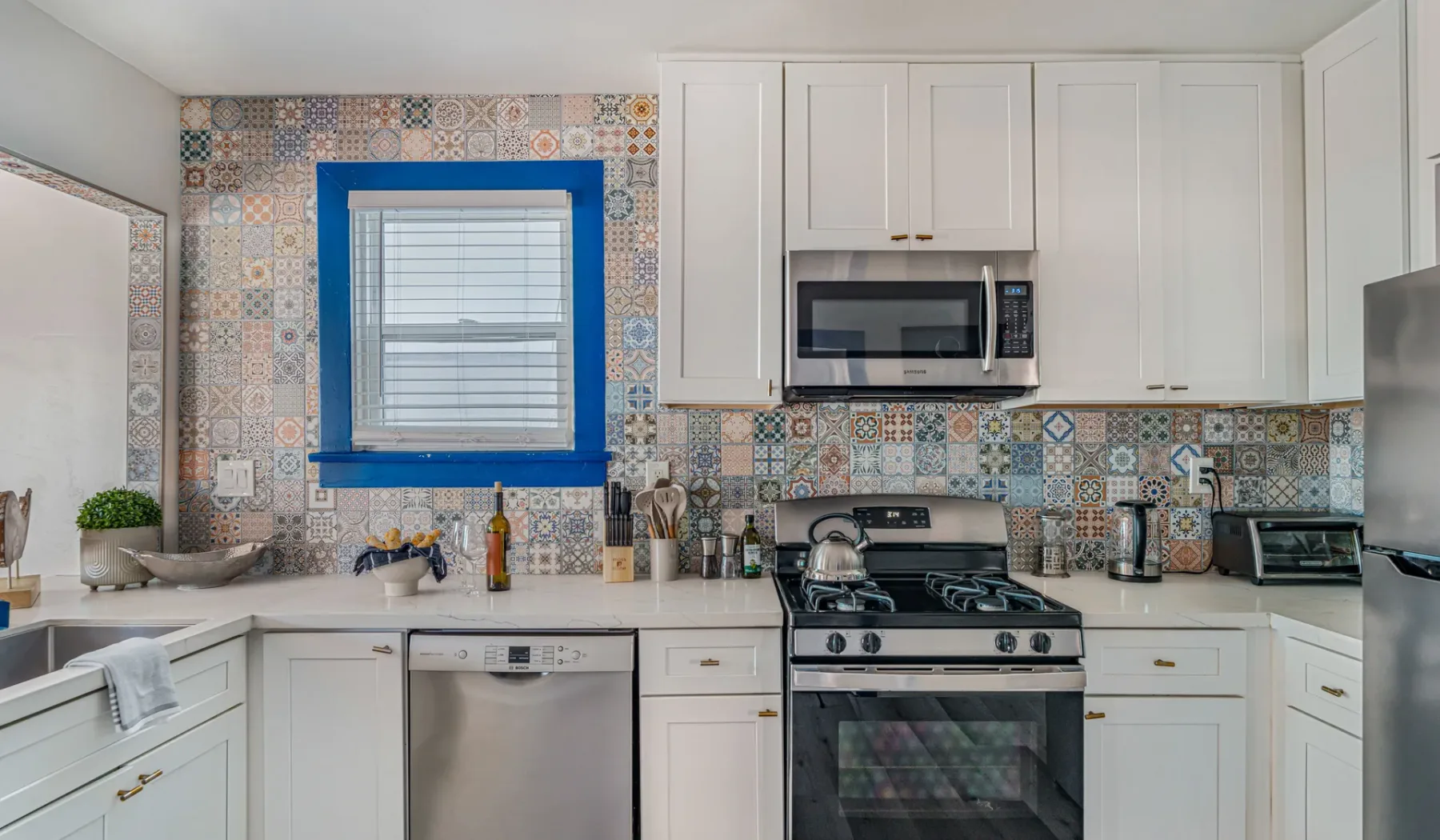 A bright kitchen with white cabinets, patterned tile, and a gas range.