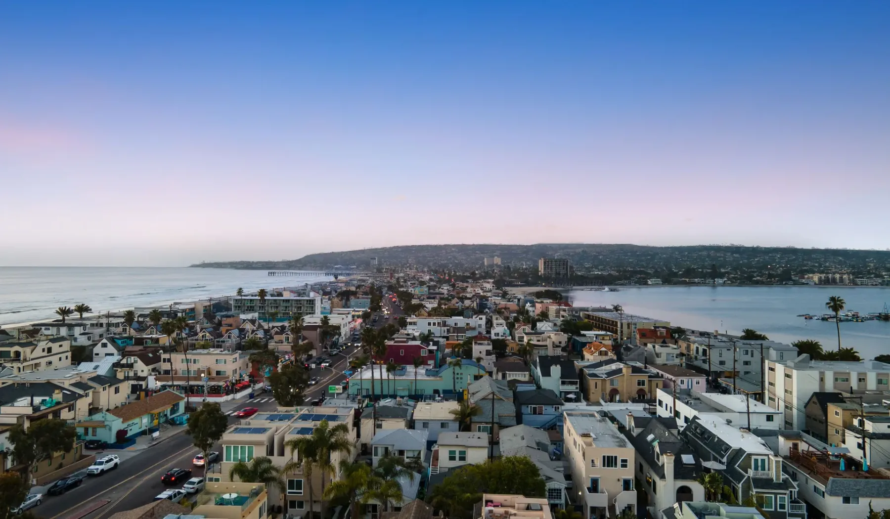 Aerial view of a coastal town with buildings between the ocean and a bay.
