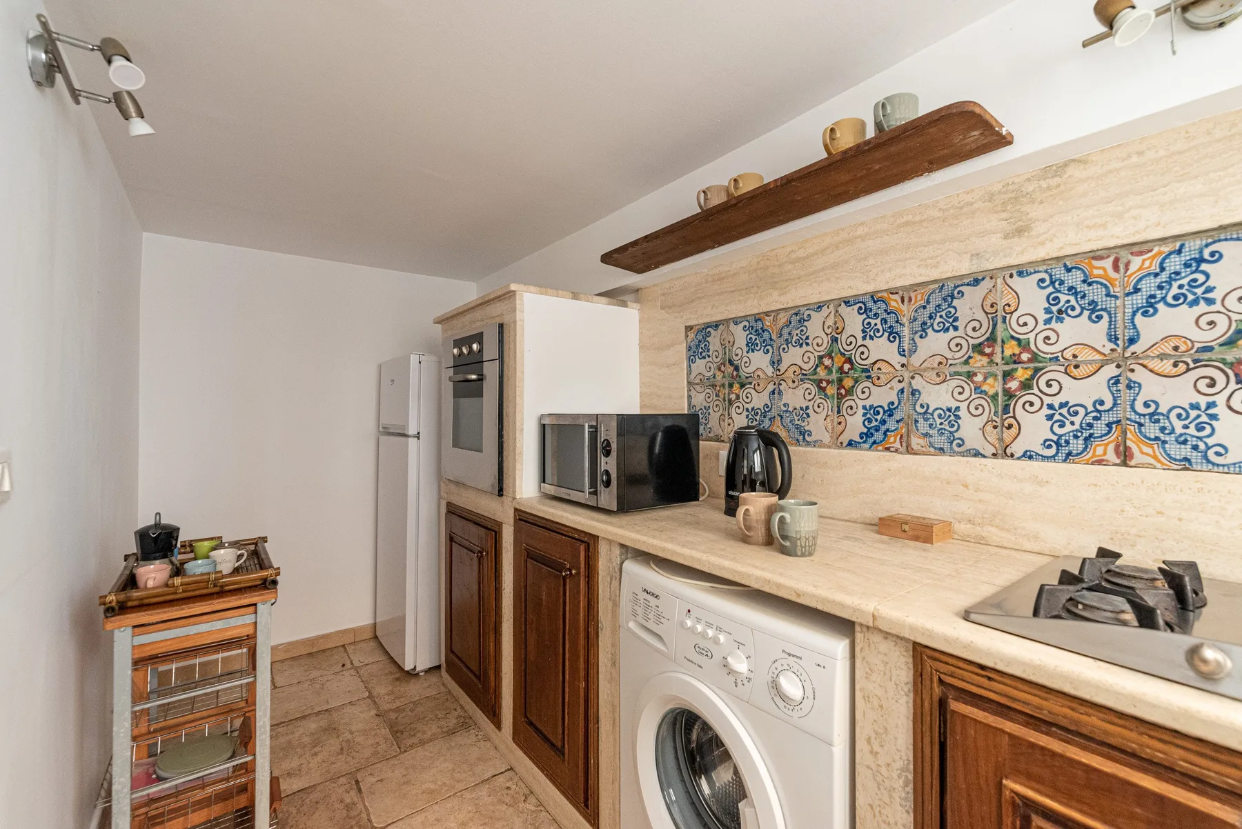 A compact kitchen with wooden cabinets, a washing machine, and a patterned tile backsplash.