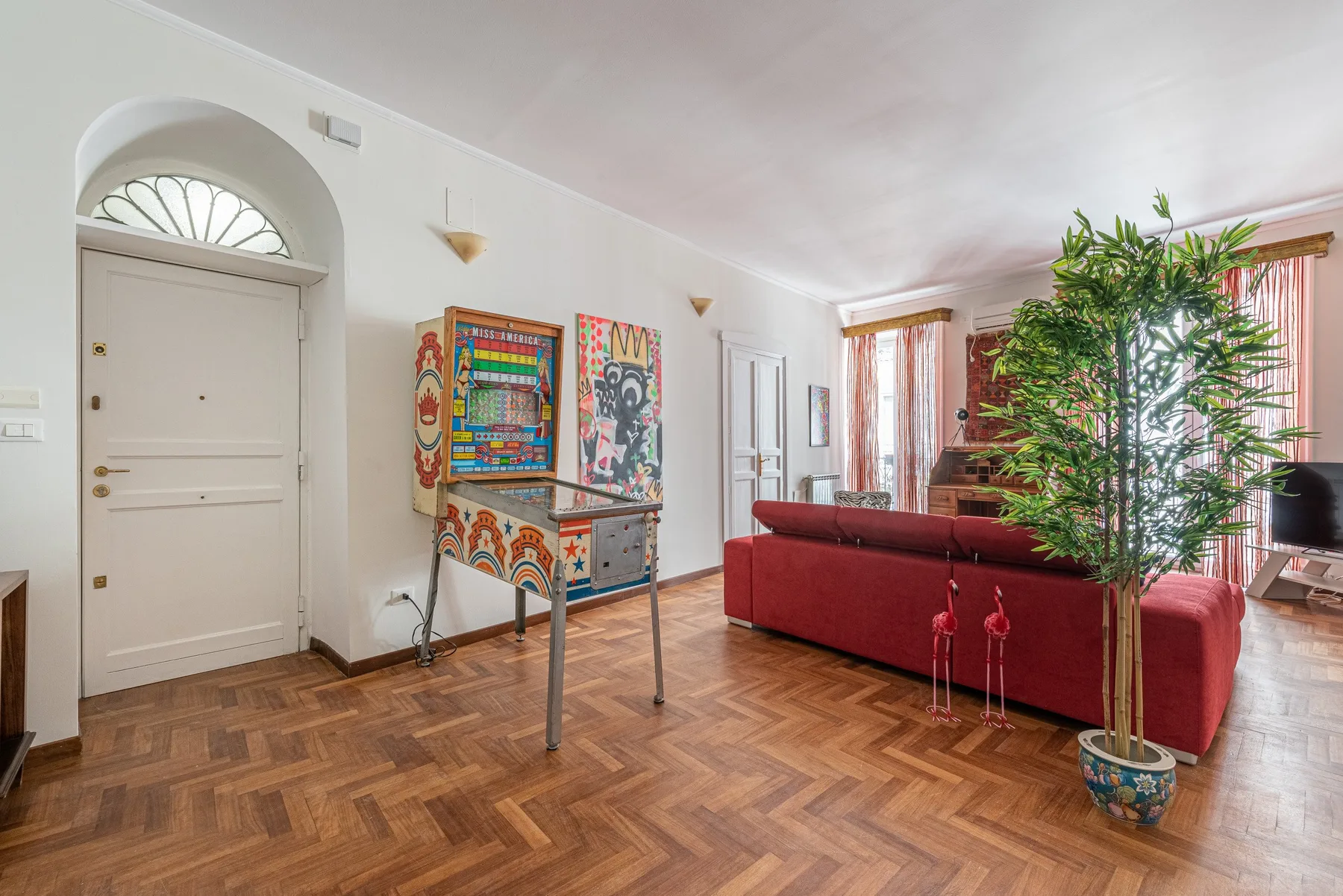 Living room with red seating, colorful wall art, and a potted plant.