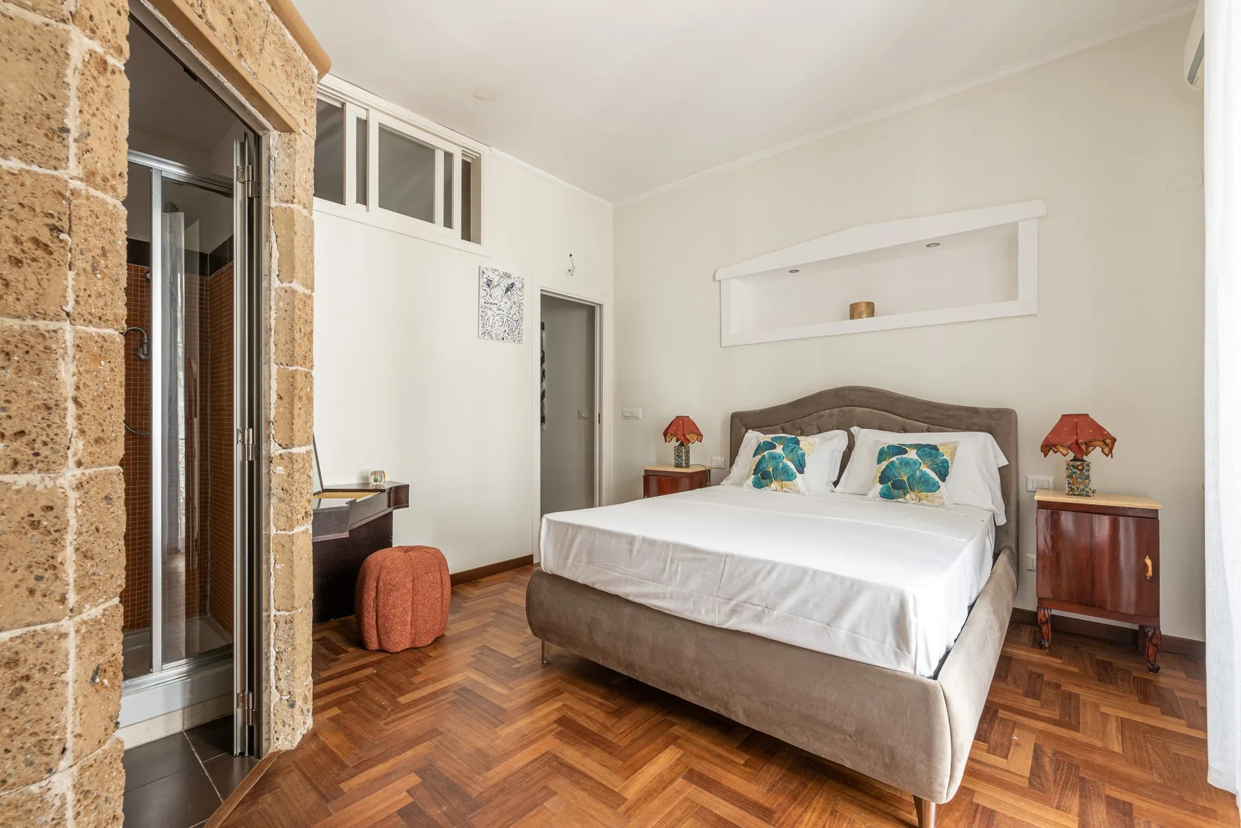 A bedroom with a double bed, bedside tables, and patterned wood flooring.