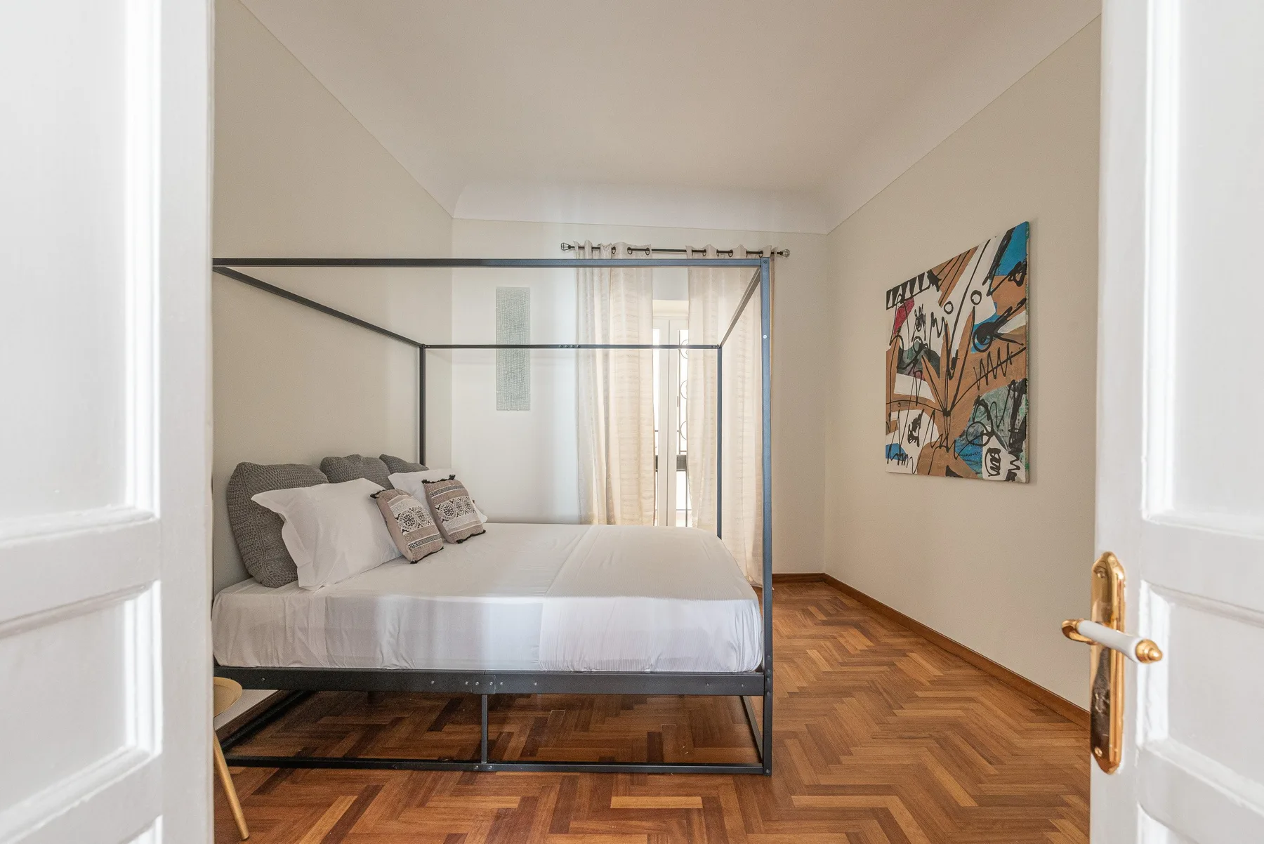 A bedroom with a canopy bed and abstract artwork on the wall.