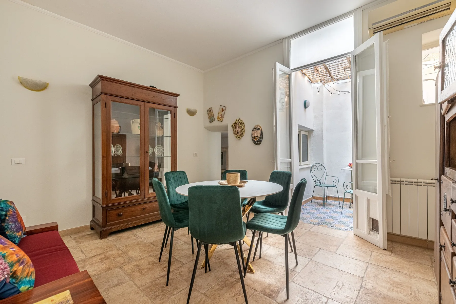 A dining area with a round table and green seating beside open doors.