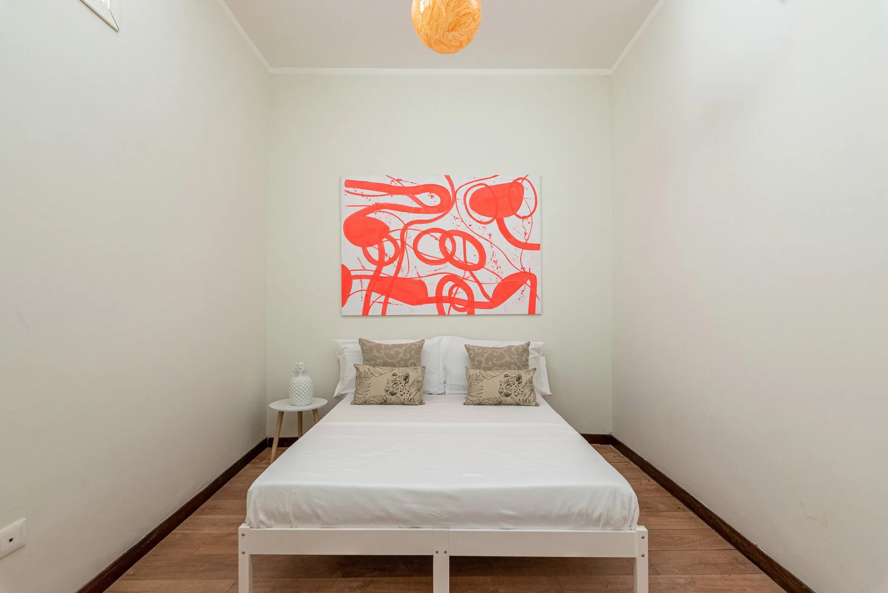 A bedroom with a neatly made bed beneath a red abstract artwork.