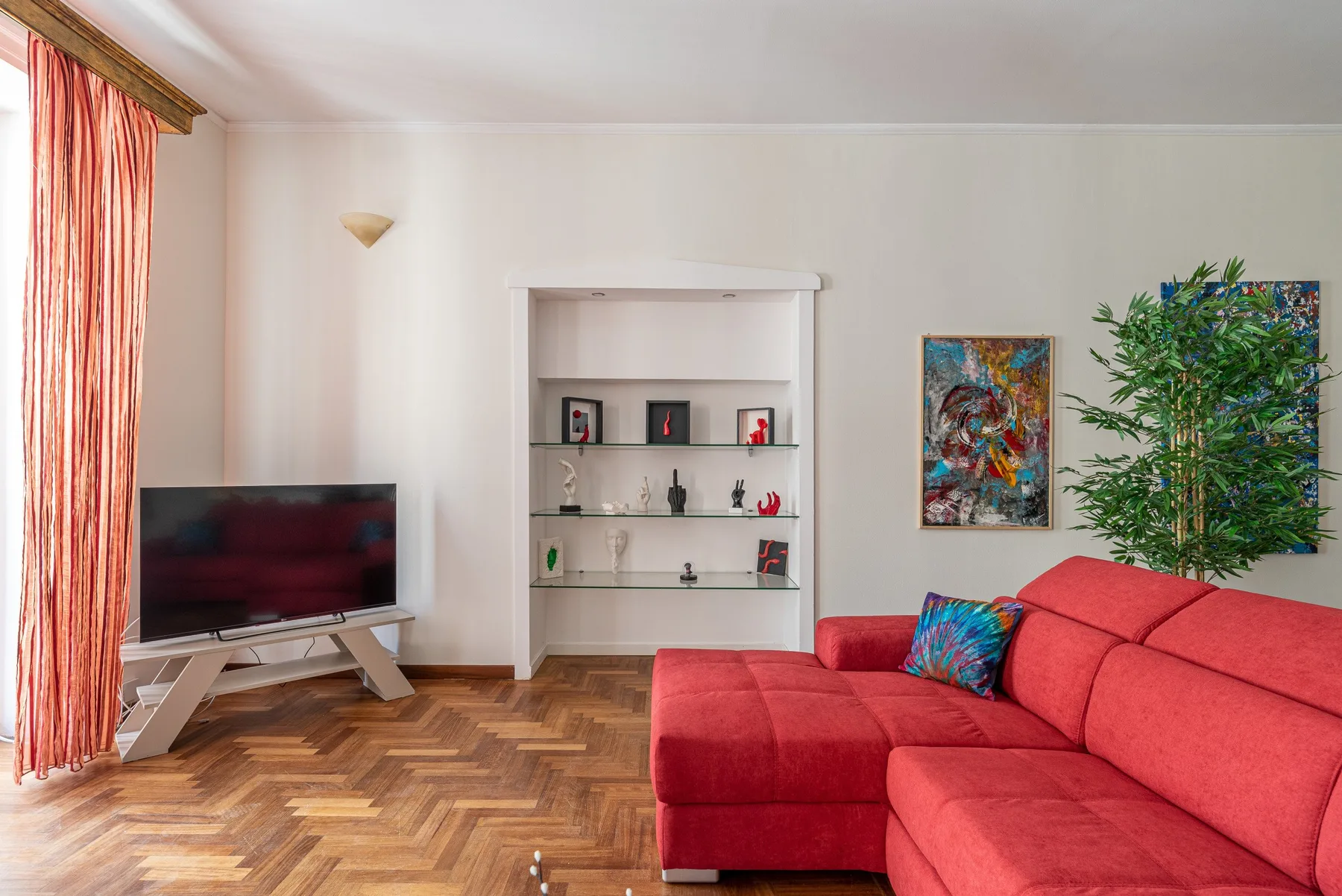 A living room with red seating, a television, and shelves displaying decorative objects.