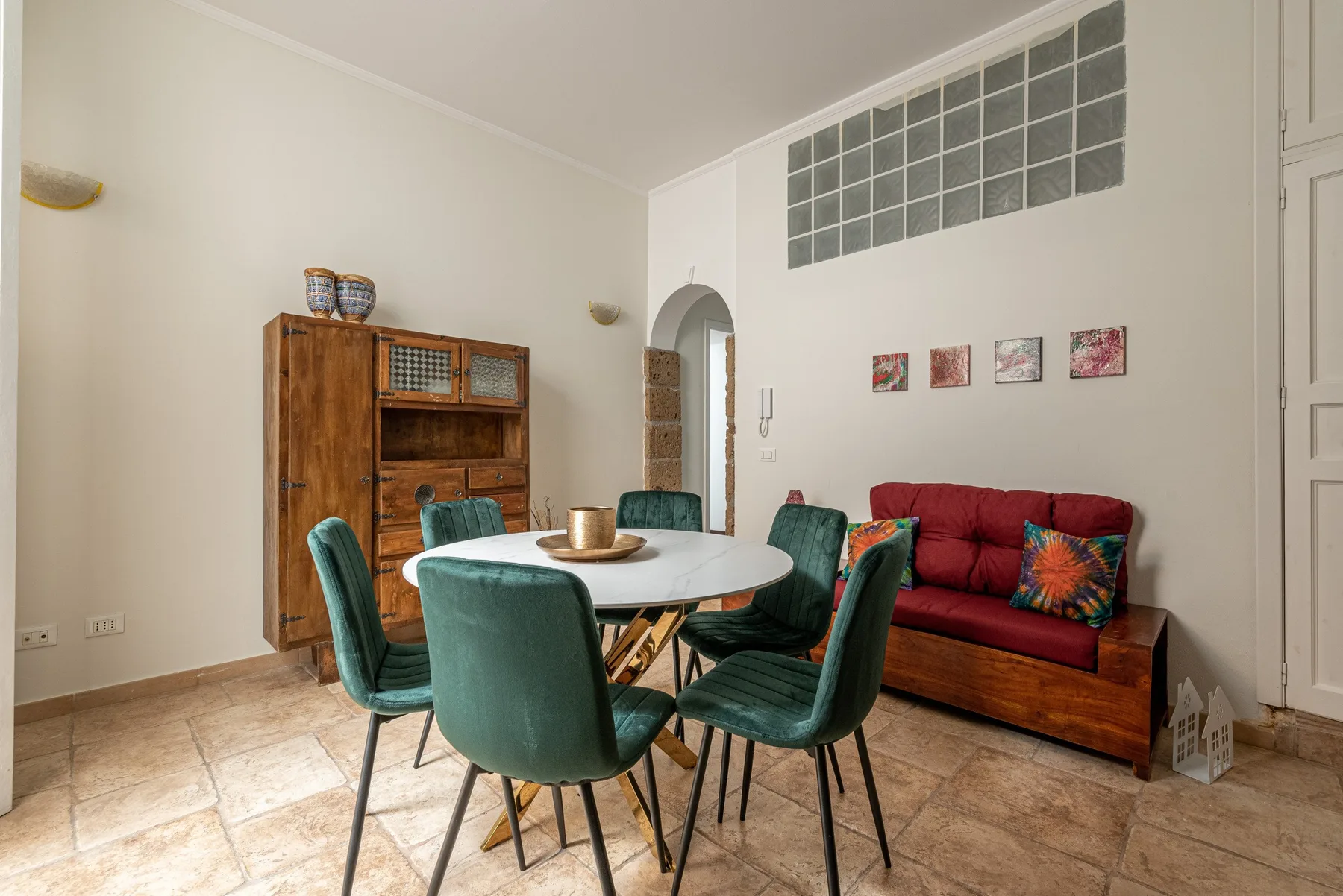 A dining area with a round table and green seating beside a red sofa.