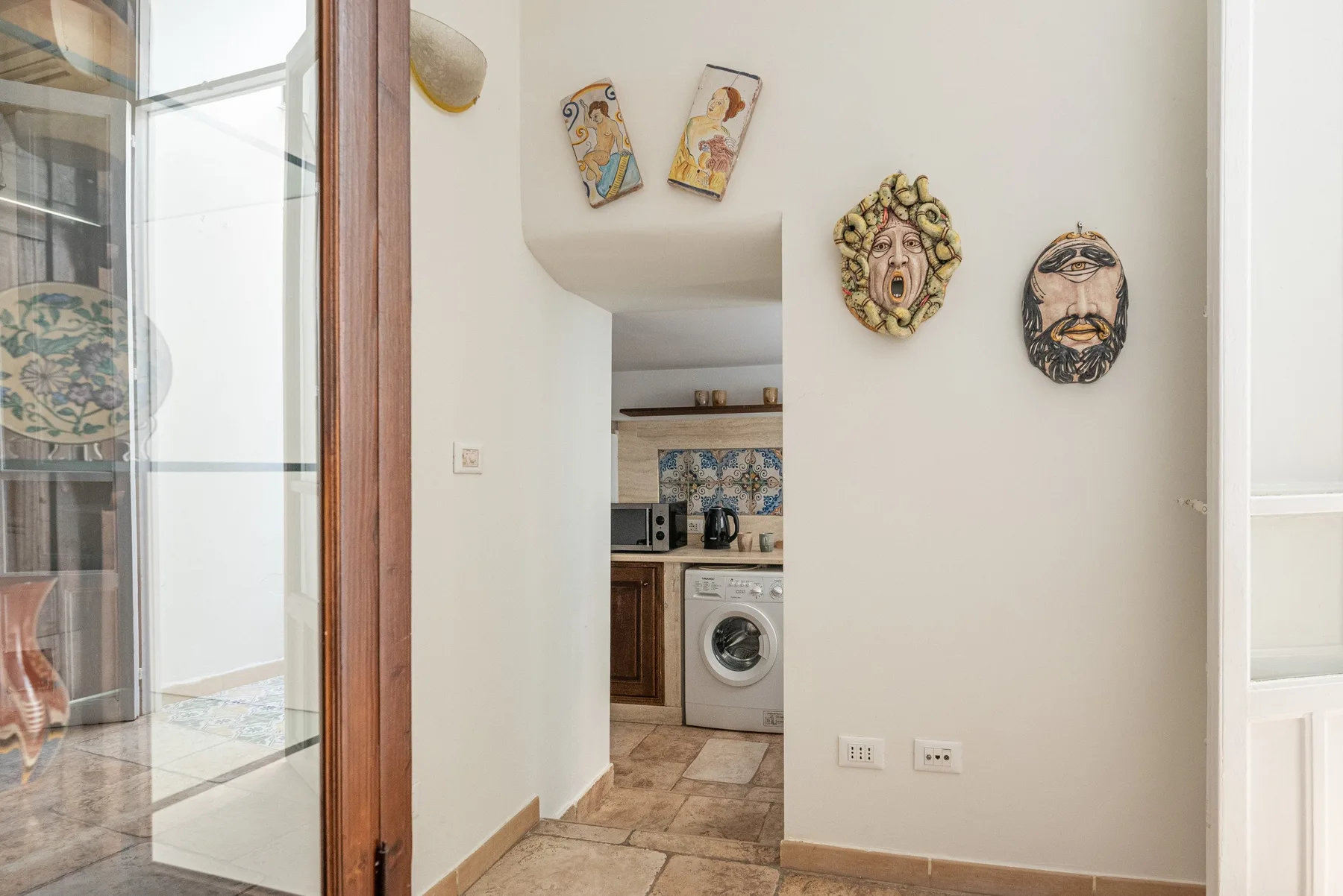 A bright hallway opens onto a compact kitchen with patterned tile and a washing machine.