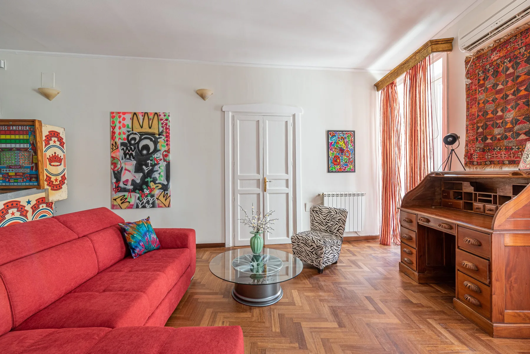 A colorful living room with red seating, a glass coffee table, and a wooden desk.