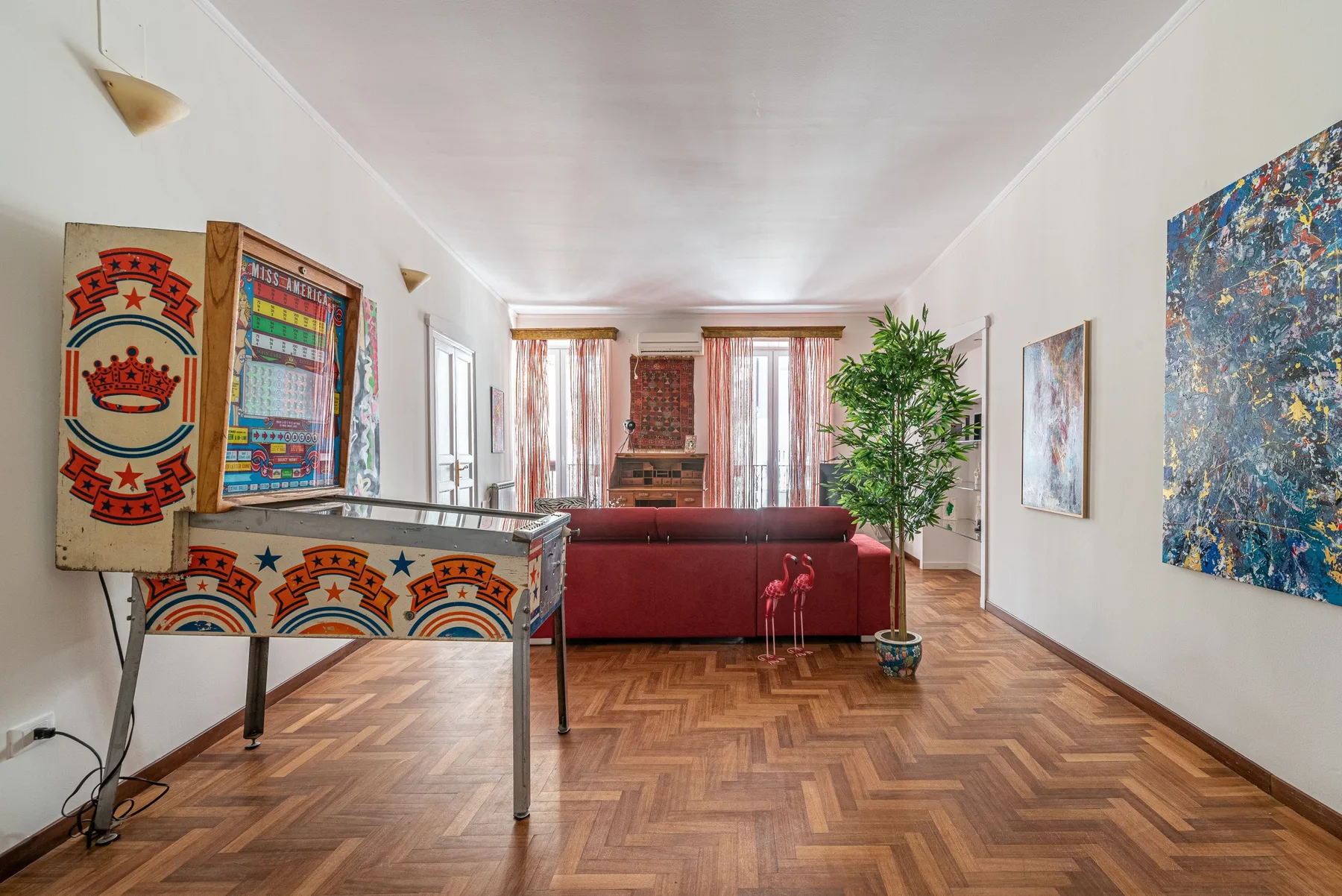 A living room with a red sofa, colorful artwork, and a potted plant.