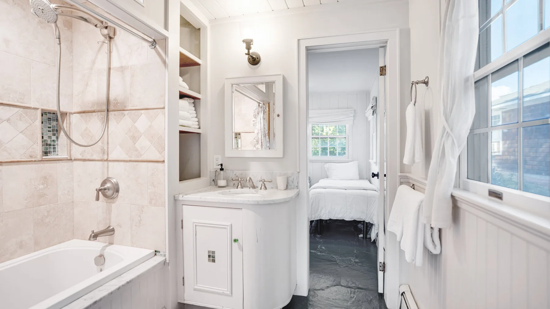 A bright bathroom with a bathtub, vanity, and doorway to a bedroom.