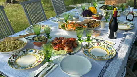 An outdoor dining table is set with plates, glassware, and a meal.