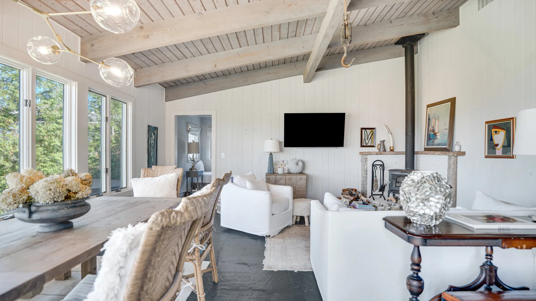 A bright living room with white seating, large windows, and a television.