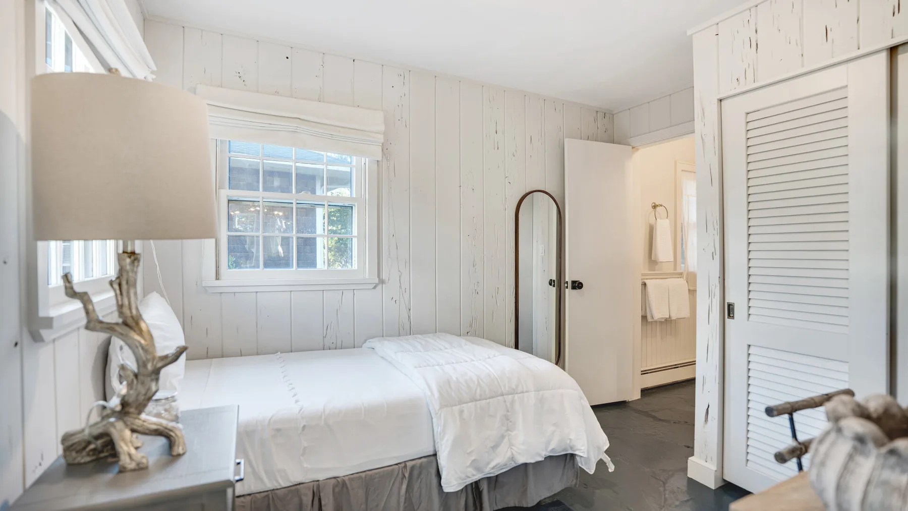 A bright bedroom with a neatly made bed and white paneled walls.