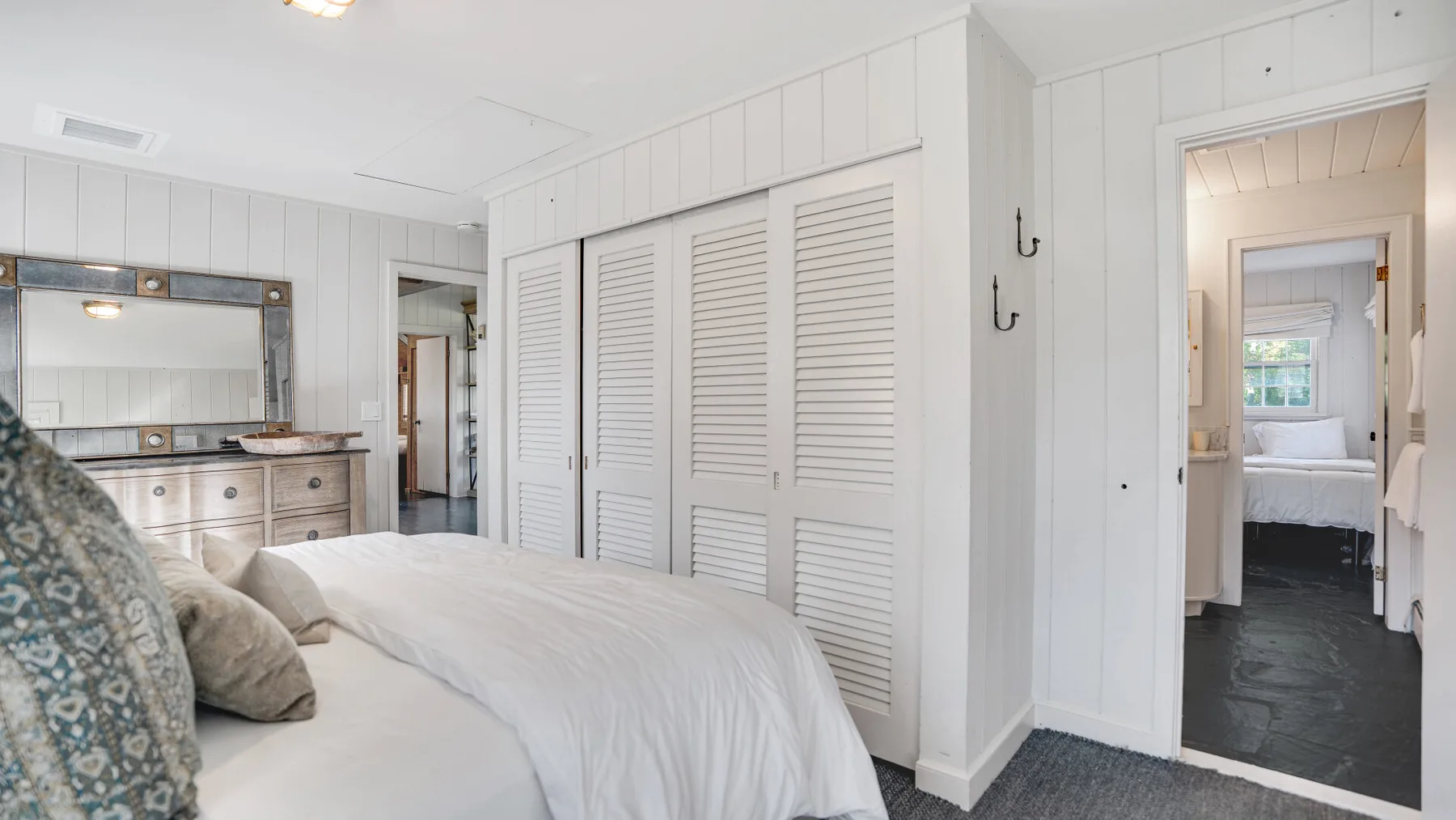 A bright bedroom with a large bed and white louvered closet doors.