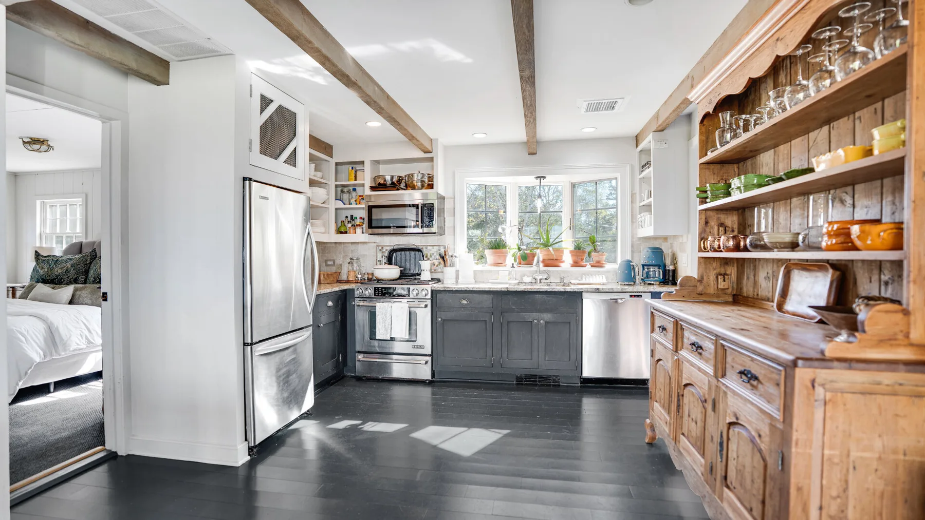 A bright kitchen with dark cabinets, stainless steel appliances, and wooden shelves.