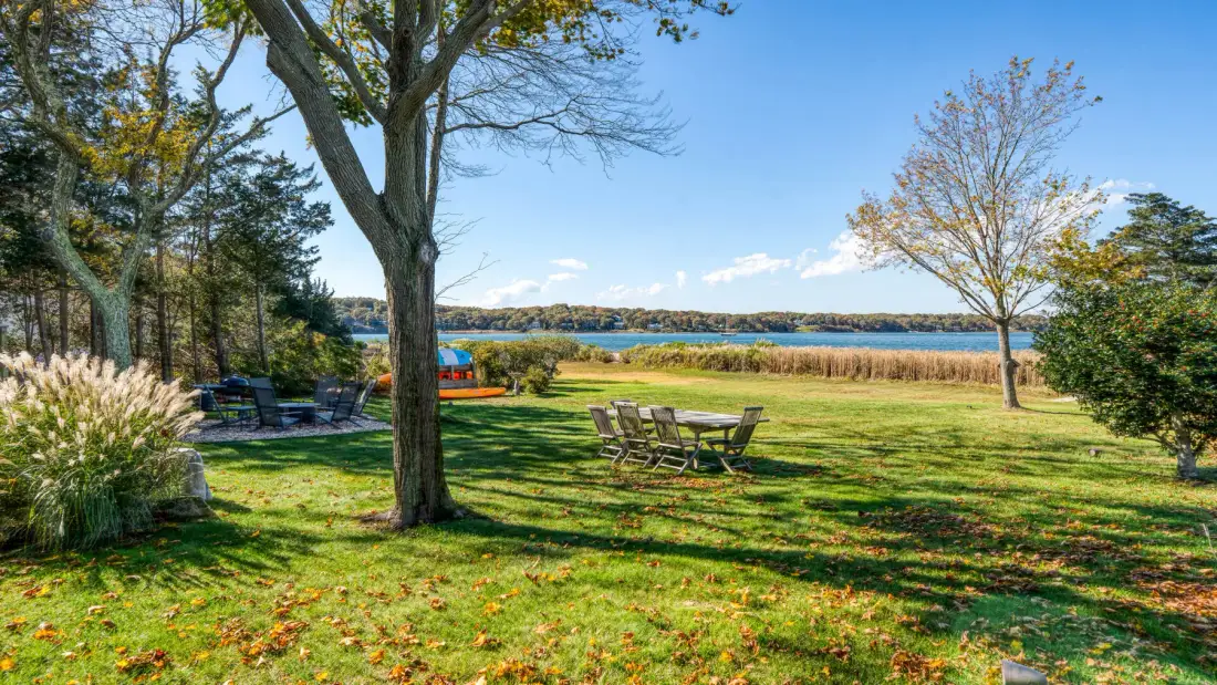 A grassy lakeside yard with outdoor seating and trees.