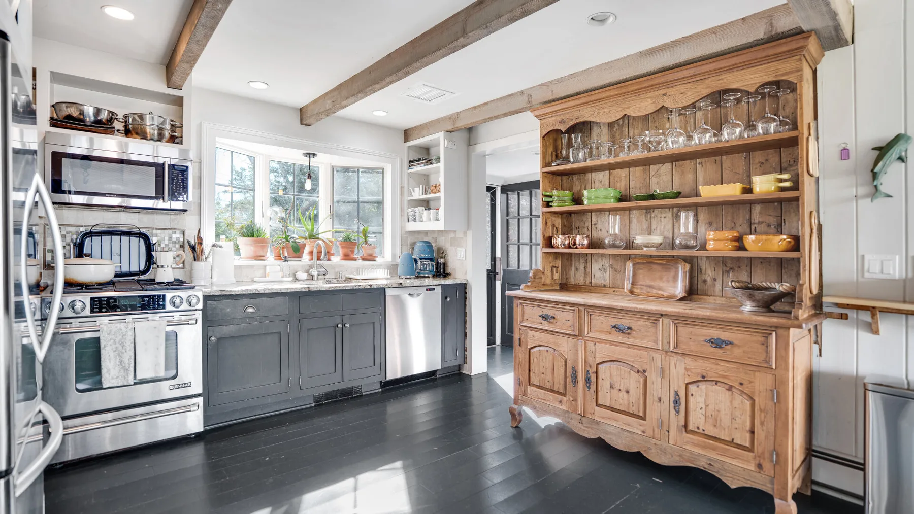 A bright kitchen with dark cabinets, stainless steel appliances, and a wooden hutch.