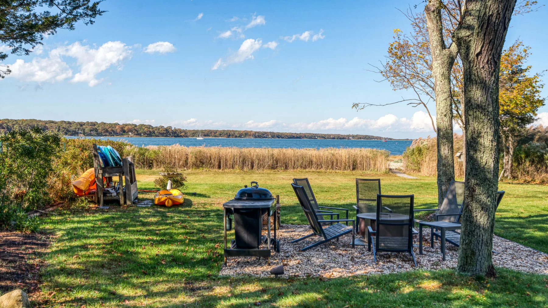 Outdoor seating and a grill sit on a grassy lakeside area.