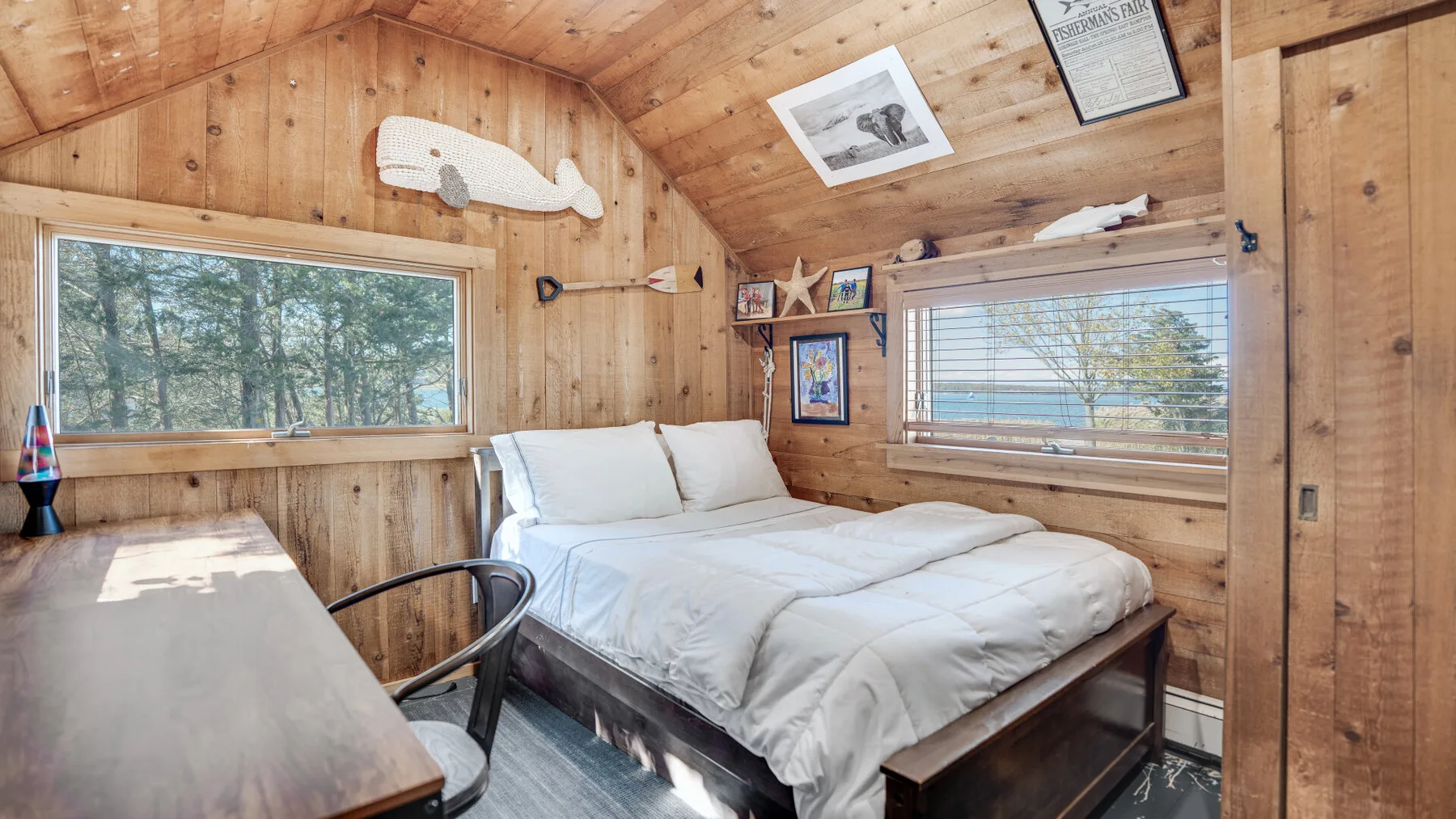 A wood-paneled bedroom has a bed beneath windows overlooking trees and water.