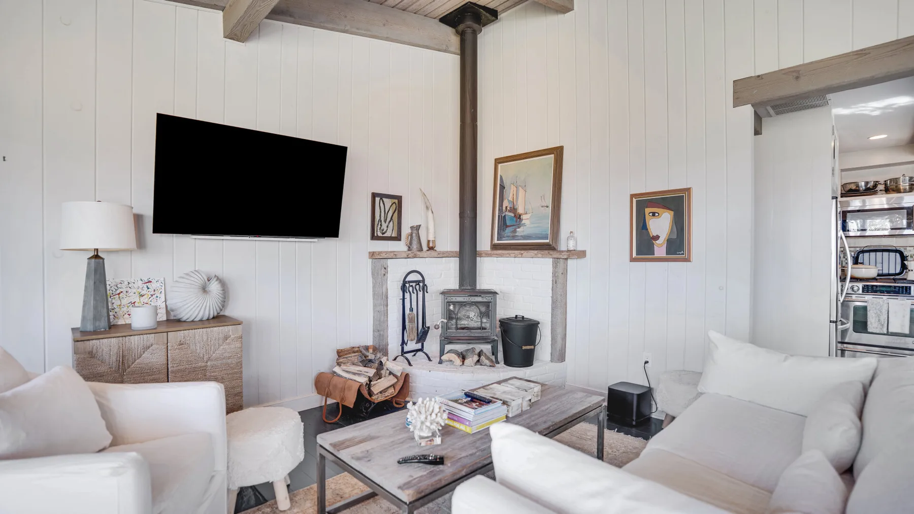 A bright living room with white seating, a television, and a fireplace.