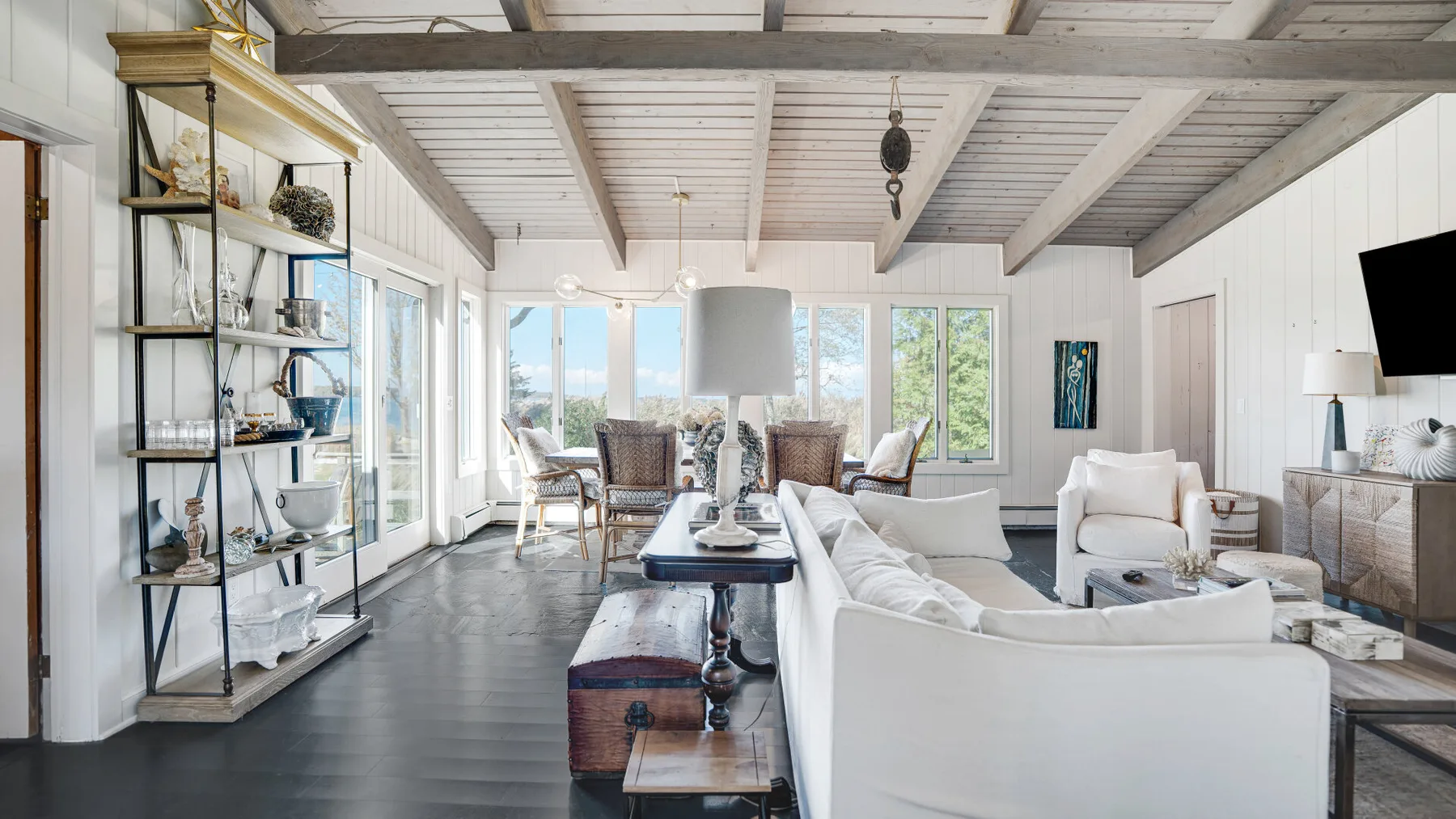 A bright living room with white seating, large windows, and exposed ceiling beams.
