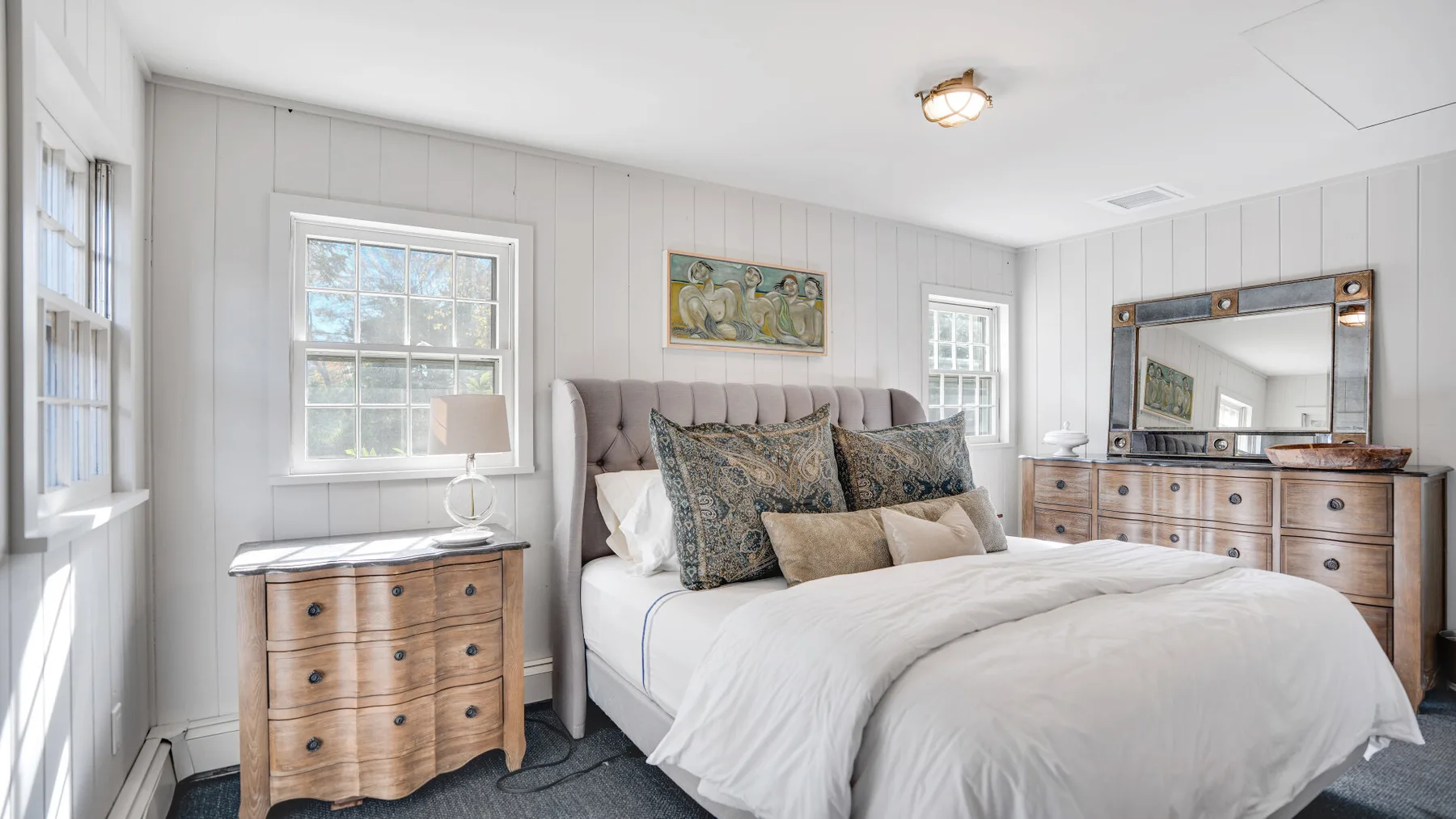 A bright bedroom with a neatly made bed and a wooden dresser.