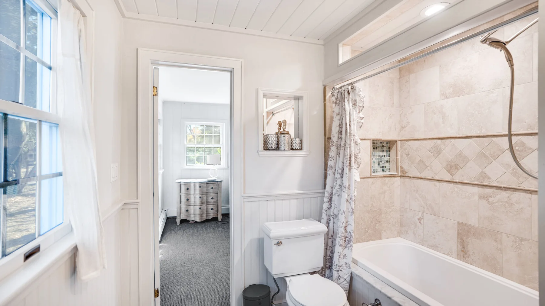 A bright bathroom with a bathtub and shower beside an open doorway.