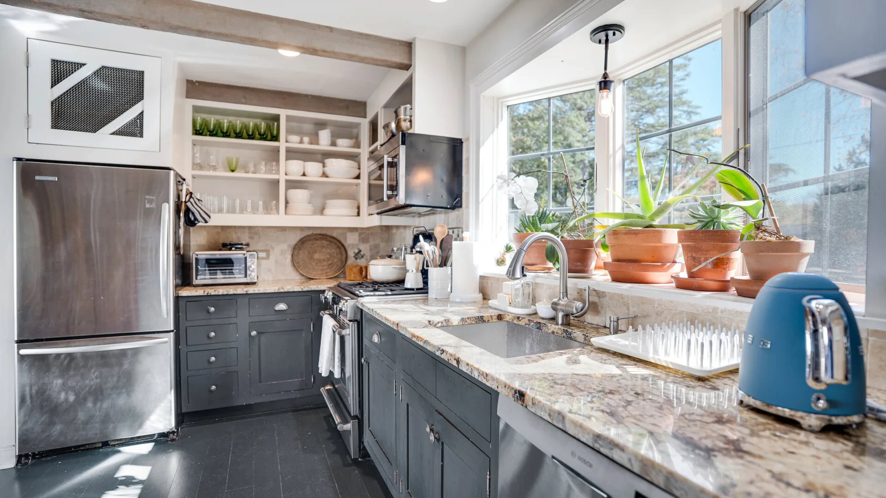 A bright kitchen with dark cabinets, a stone countertop, and large windows.